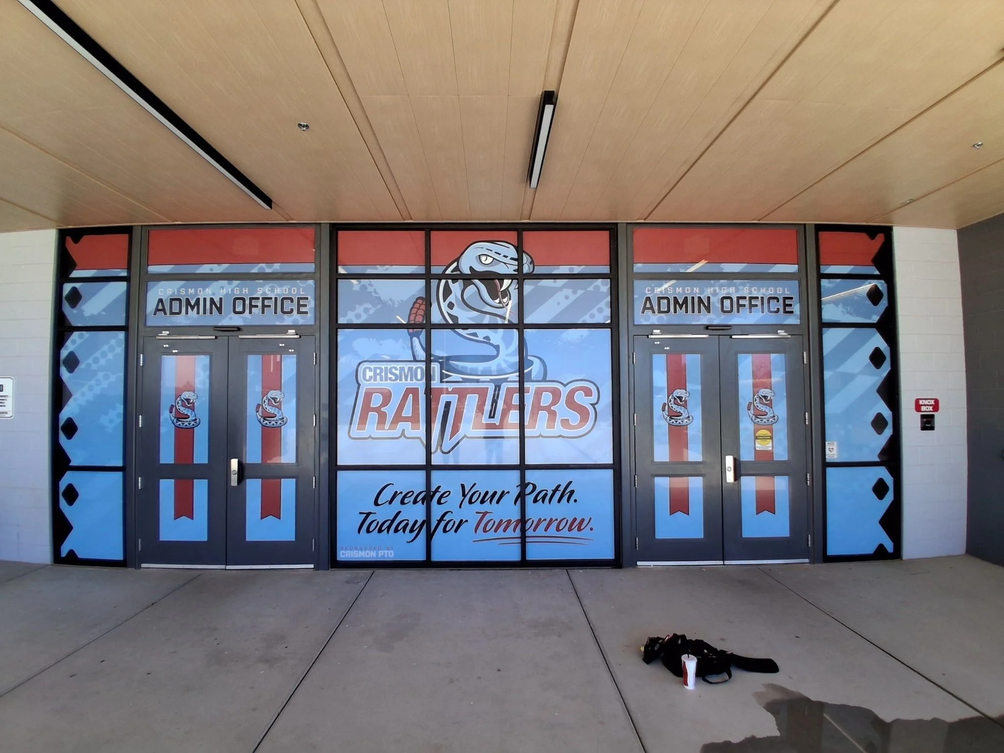 School entrance doors with banner for Crisman High School Rams, featuring a snake mascot, motivational quote, and school information.