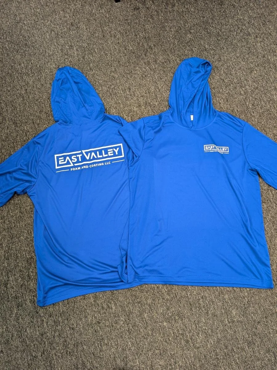 Two blue hooded shirts with the logo 'East Valley Foam and Coating LLC' laid flat on a carpeted floor.