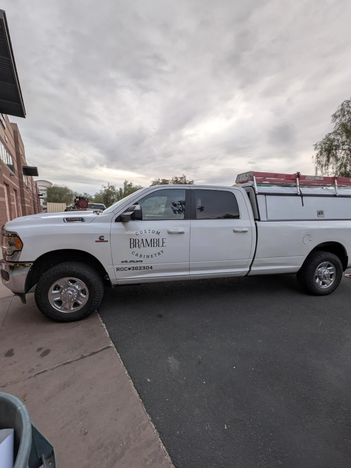 A white service pickup truck with the logo 'Custom Bramble Cabinetry' parked next to a brick building and overcast sky.