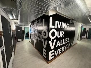 Corner wall with the word 'LOVE' vertically and the phrase 'LIVING OUR VALUES EVERYDAY' horizontally in bold white letters on a black background.