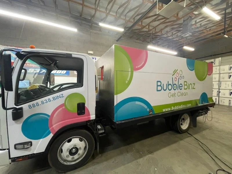 A cleaning truck with Bubble Binz branding inside a warehouse, featuring colorful bubbles and the slogan "Get Clean."