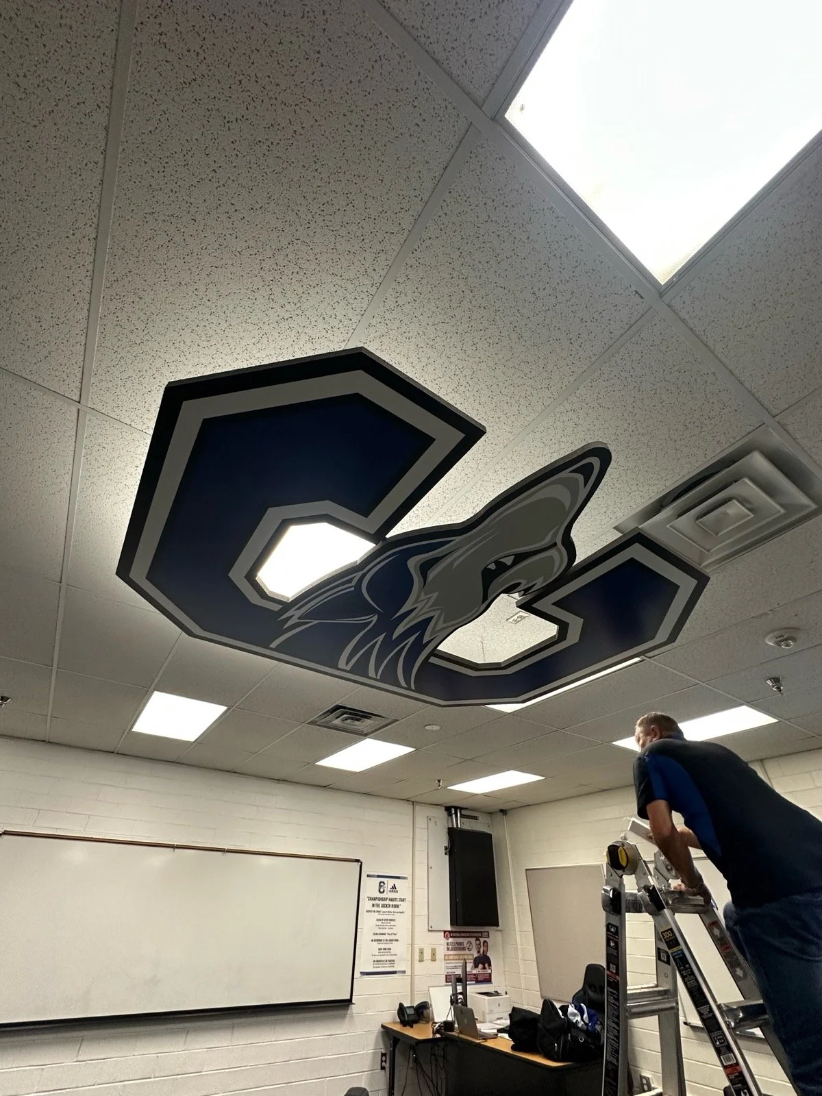 Ceiling in a classroom with a large logo of a stylized wolf head and letter 'C' attached to the ceiling.