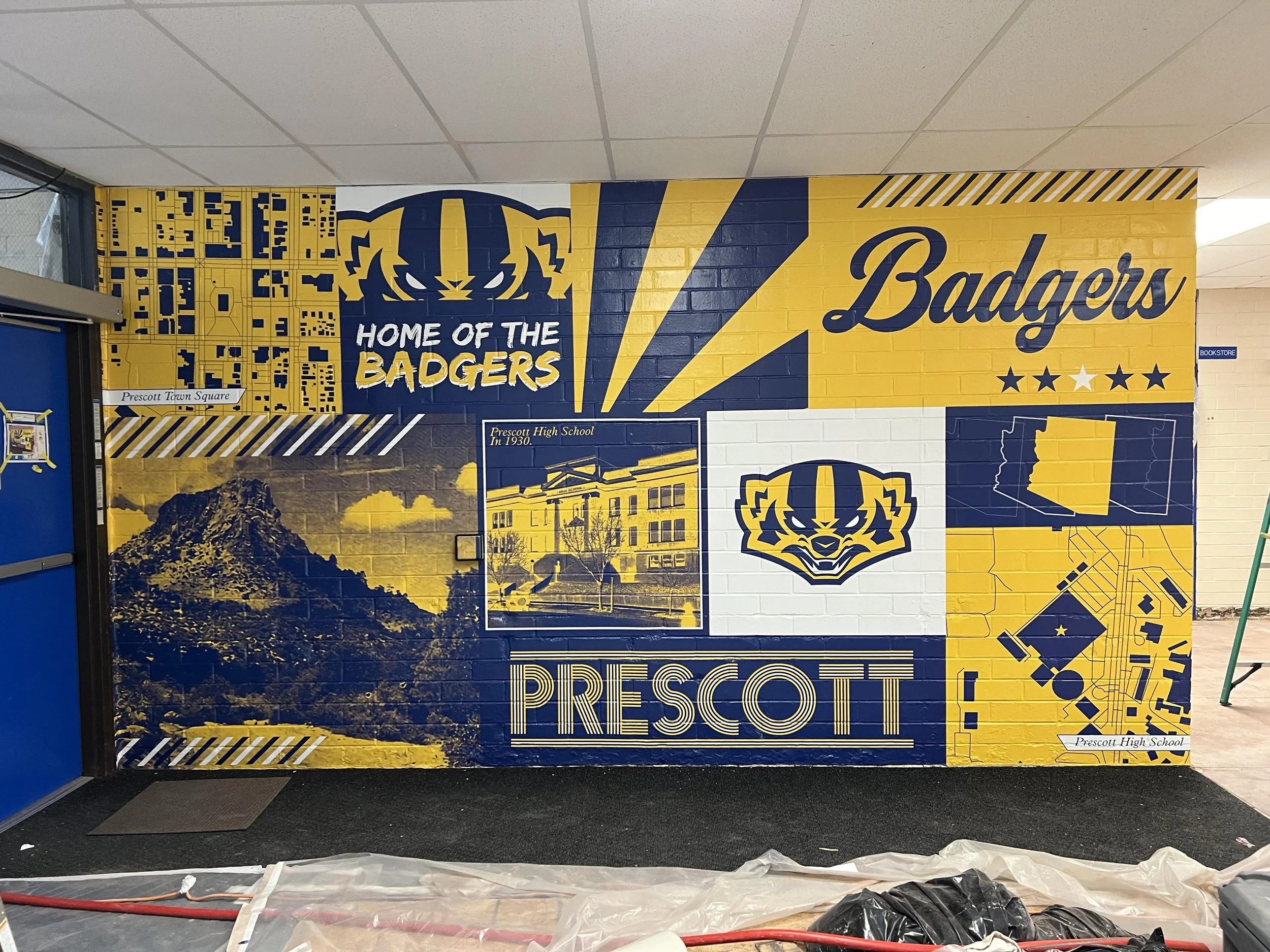 A large wall display in yellow and blue colors with the words "Home of the Badgers" and "Badgers" and images representing Prescott High School, including a mountain, a school building, and a map of Wisconsin.