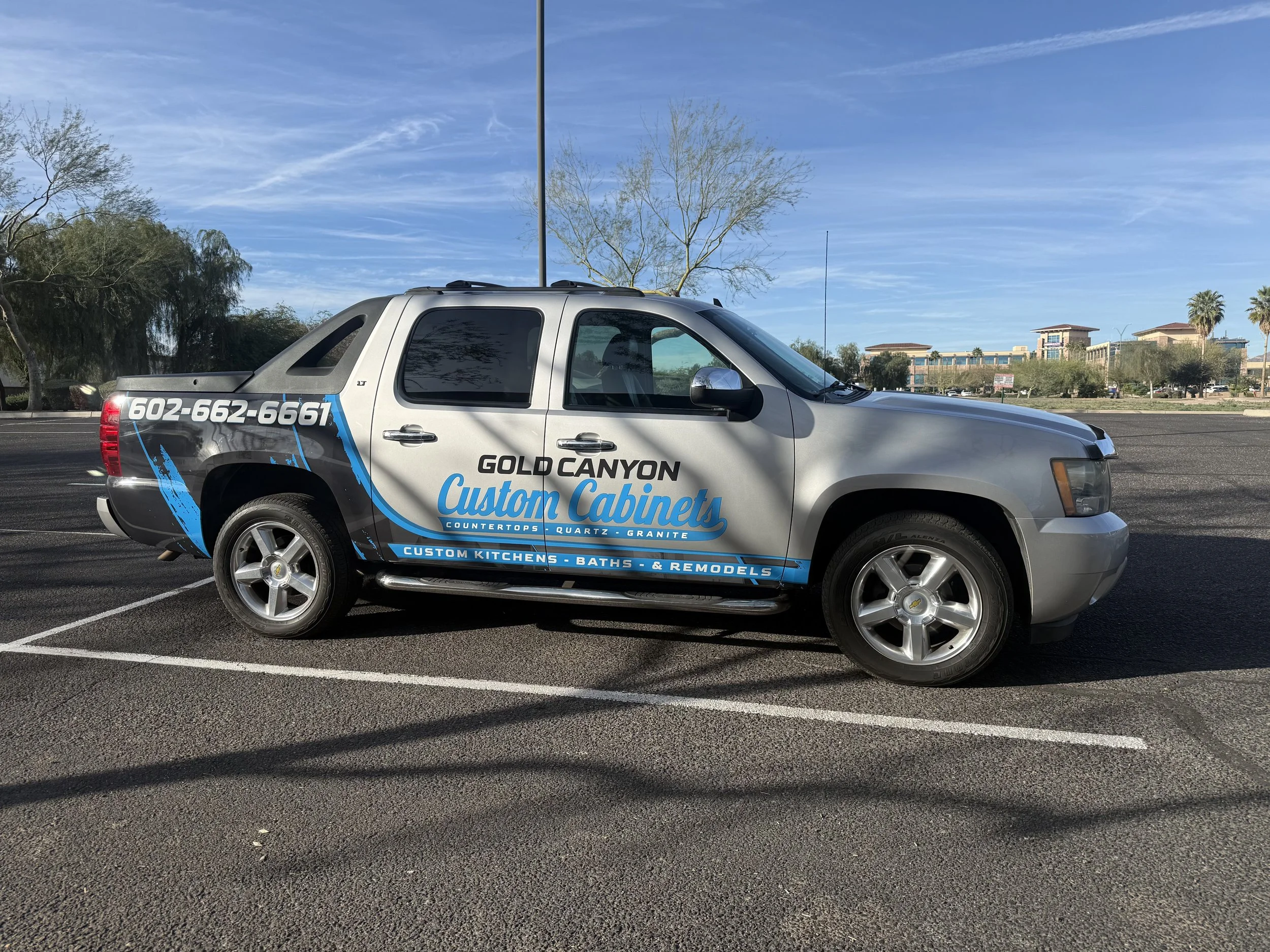 A pickup truck parked in an empty parking lot against a clear blue sky with some clouds and trees in the background.