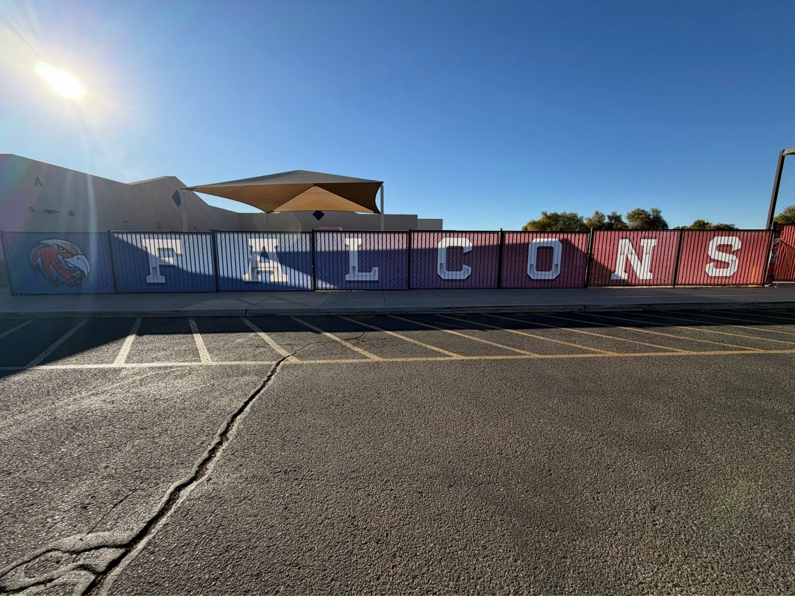 A large sign with the word "FALCONS" in white letters on a gradient blue to red background, featuring a falcon logo on the left, placed behind a black metal fence.