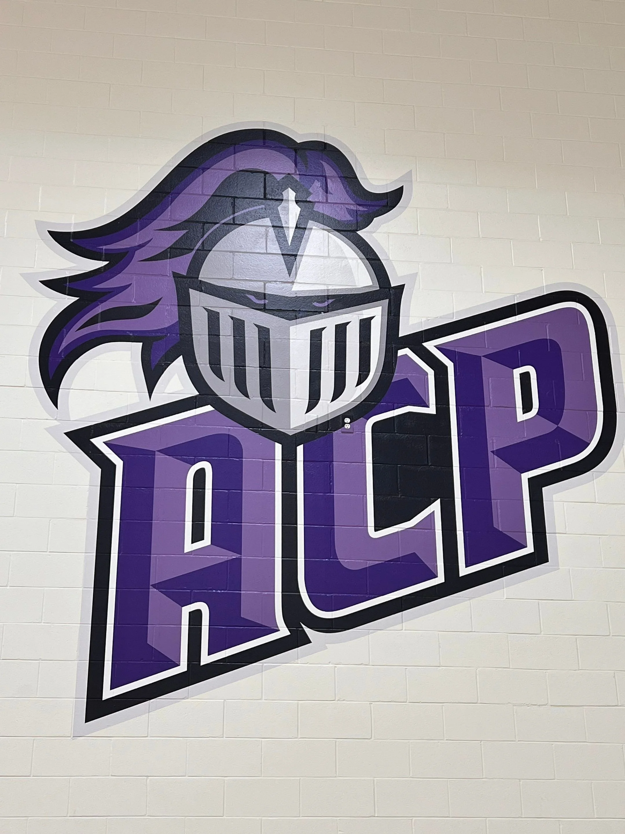 A mural of a purple and black Viking helmet with a face plate, on a purple banner with white text, mounted on a white brick wall.