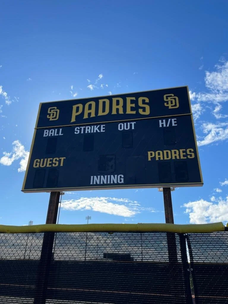Scoreboard at a baseball stadium for the San Diego Padres with no scores or inning listed, under a partly cloudy sky.