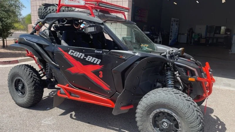 A black and red Can-Am side-by-side off-road vehicle parked outside a building with one front wheel turned to the right.