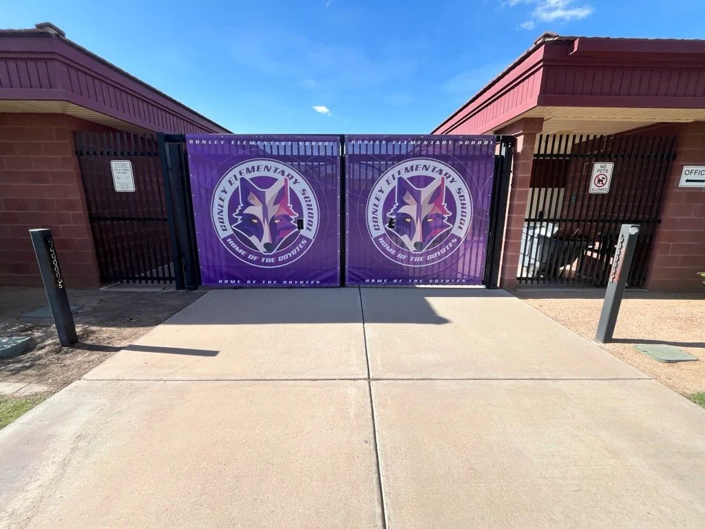 Entrance gate to Bunley Elementary School with purple banners displaying a wolf mascot and the words "Bunley Elementary School, House of the Coyotes."