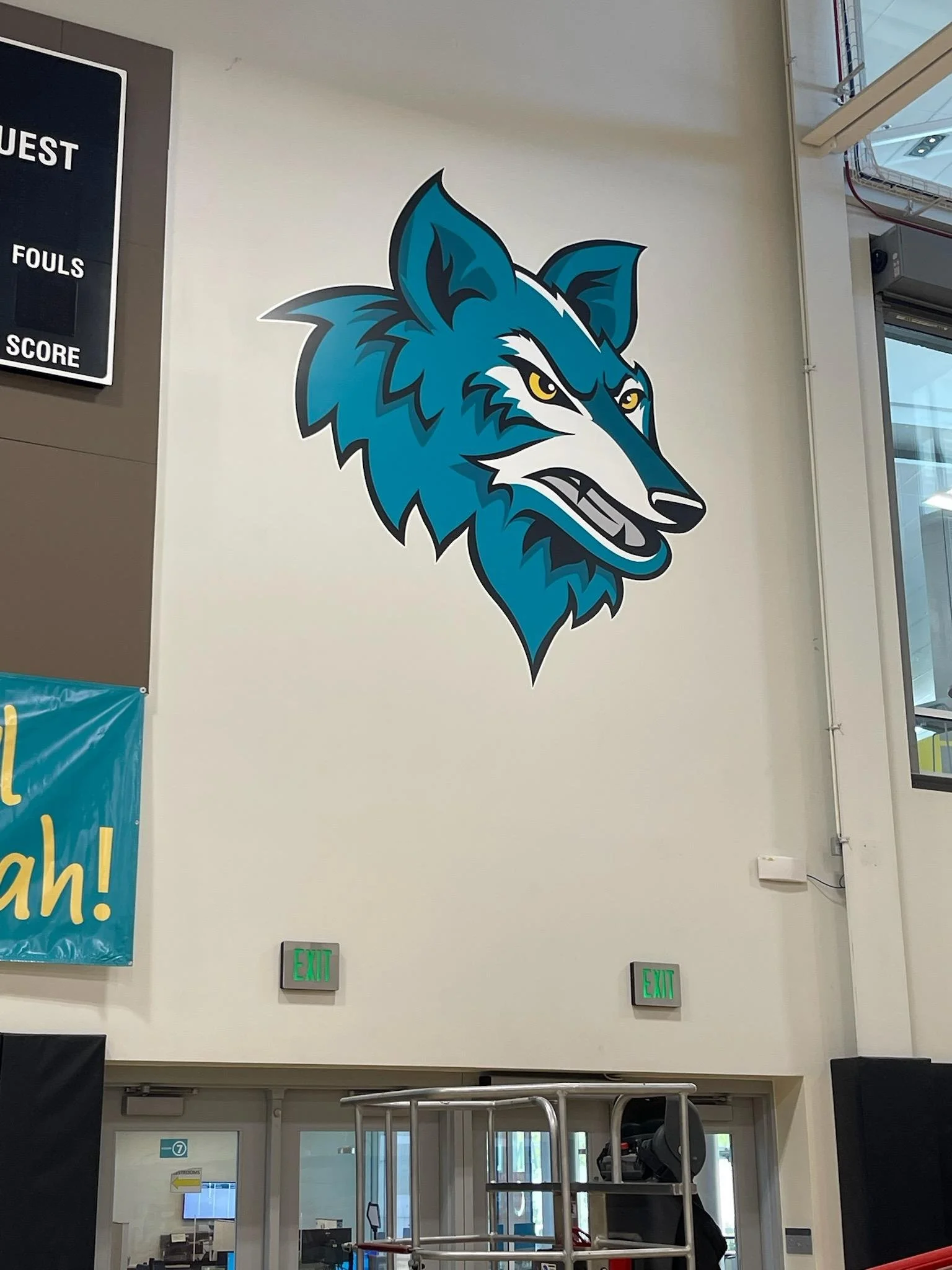 Large blue and white wolf logo on the wall of an indoor space with electrical wiring and exit signs below.