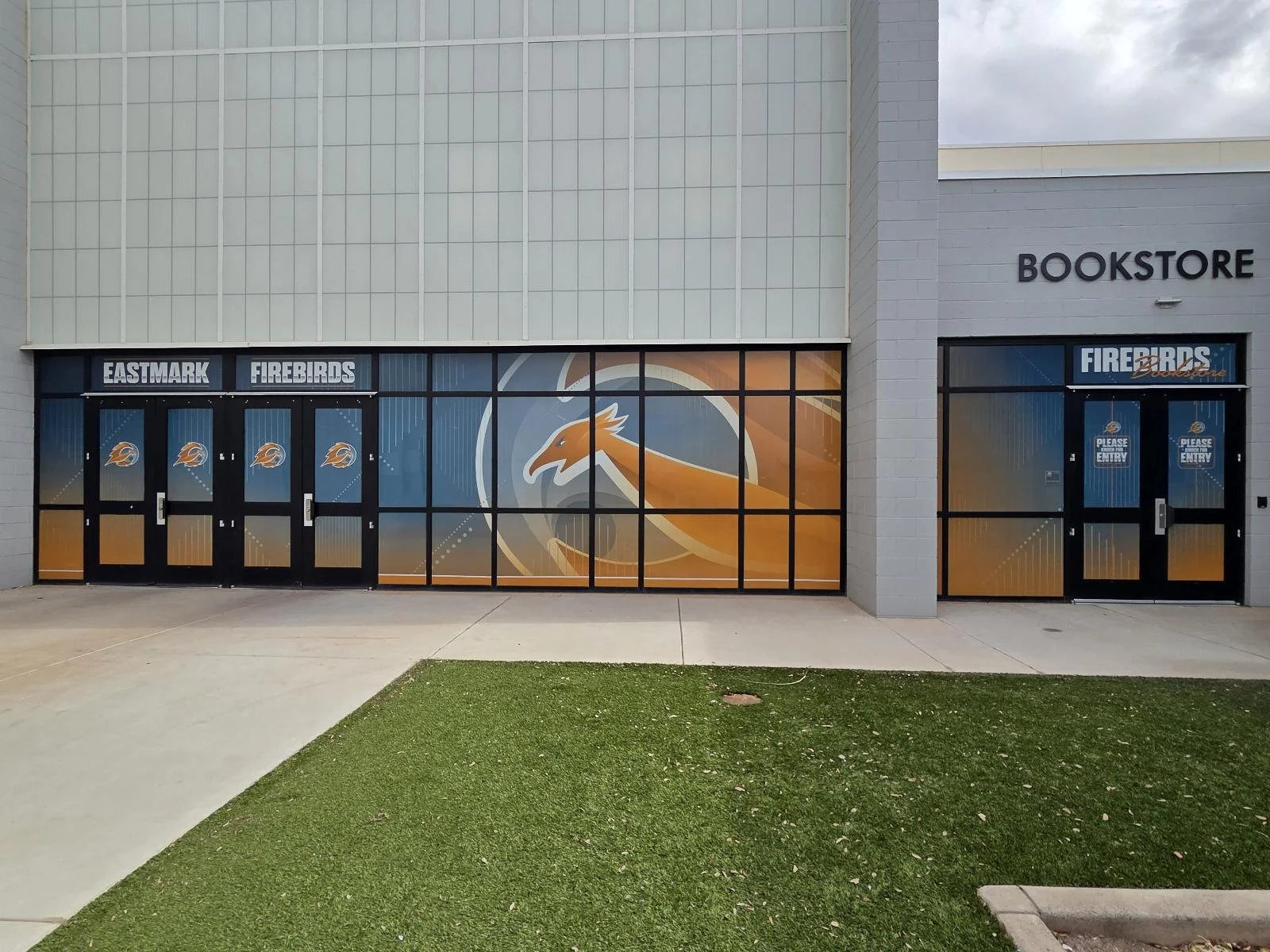 Exterior of a sports arena or stadium with signage for Eastmark Firebirds, featuring a large eagle logo on the glass doors and windows.