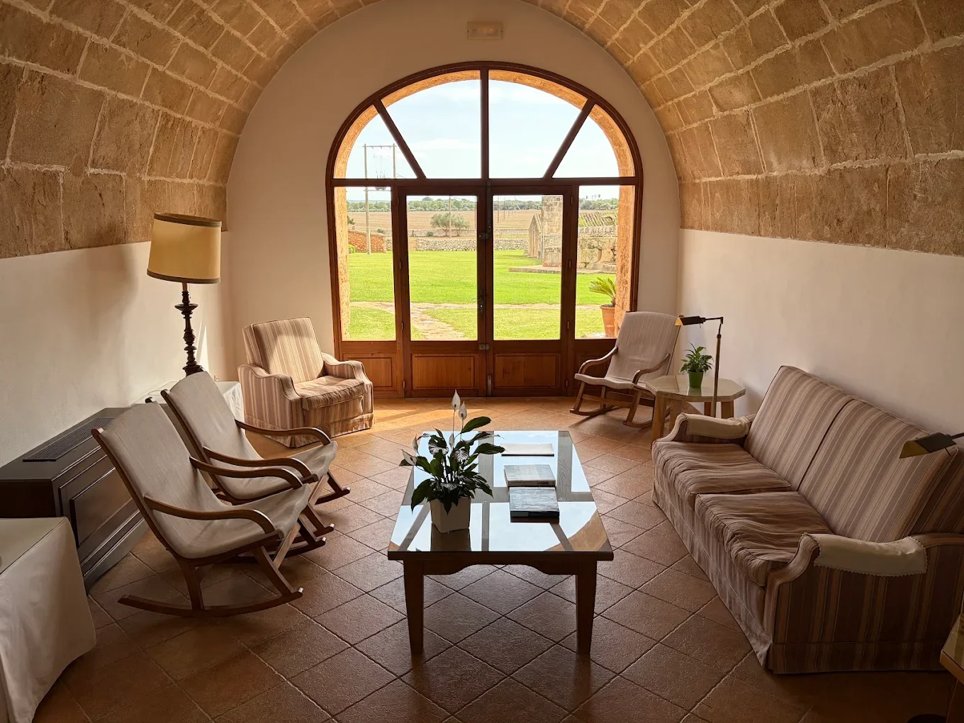 Sala de estar con sillones y mesa de madera, ventanas grandes con vista al campo, plantas decorativas