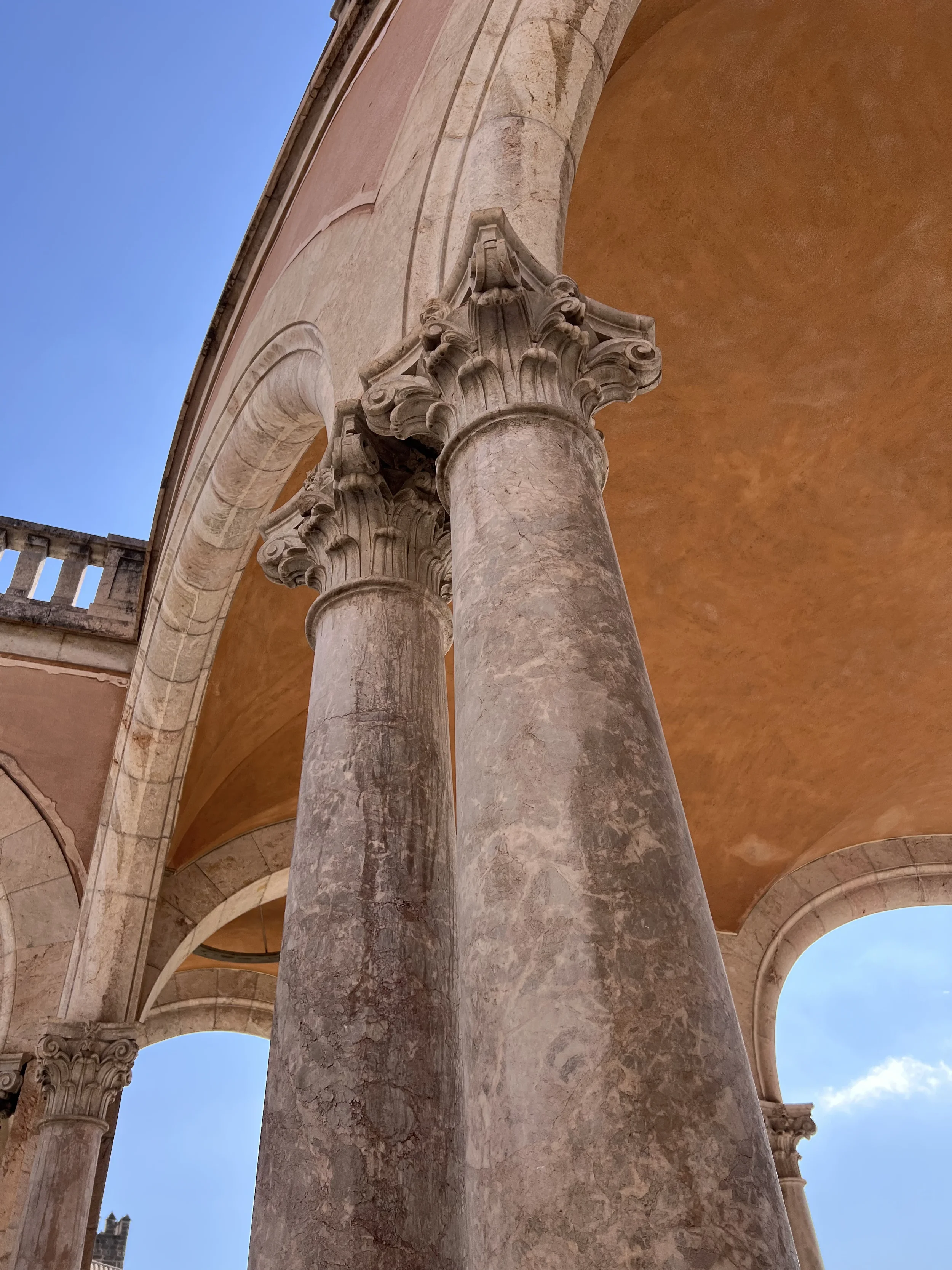 Columnas y arcos de piedra en un edificio histórico, con cielo azul visible en el fondo.