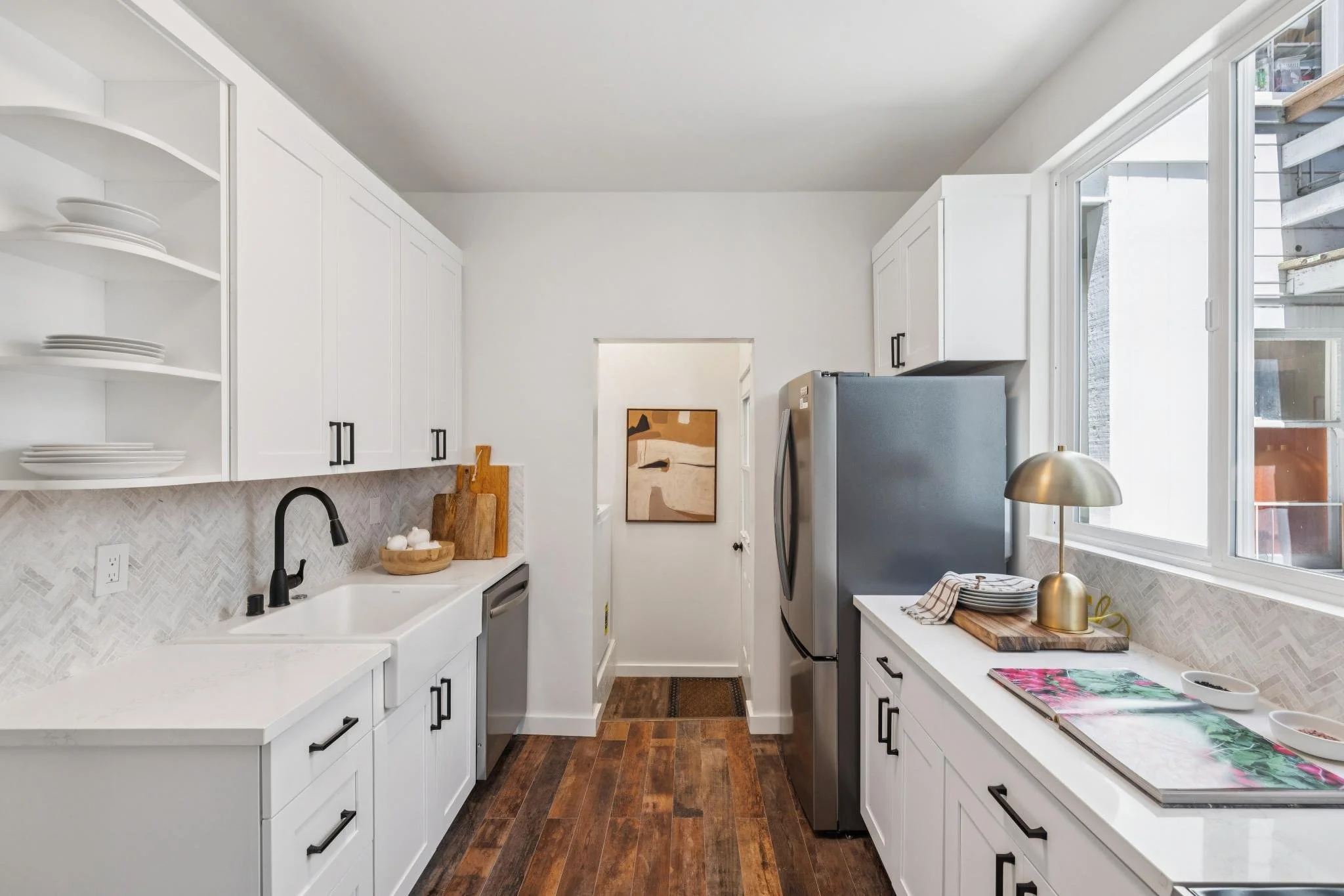 Kitchen with white cabinetry, a sink, black faucet, wood accents, stainless steel refrigerator, large window, and wooden floor.