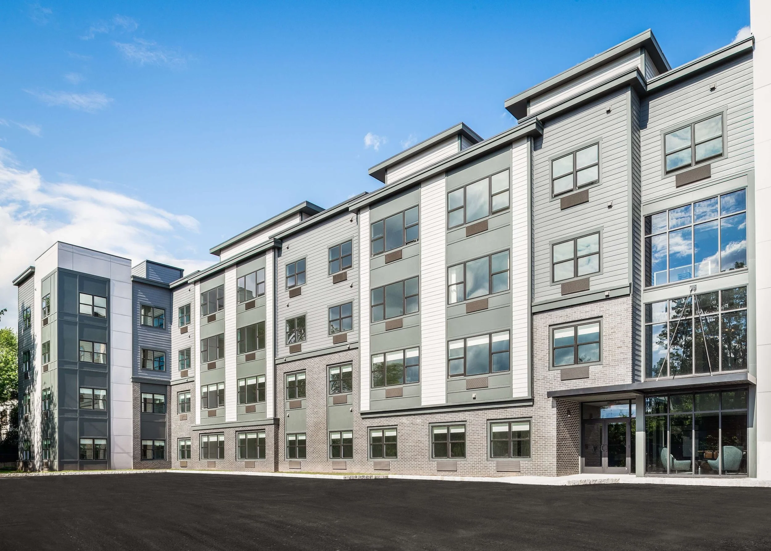 Modern multi-story residential building with large windows under a blue sky with clouds.
