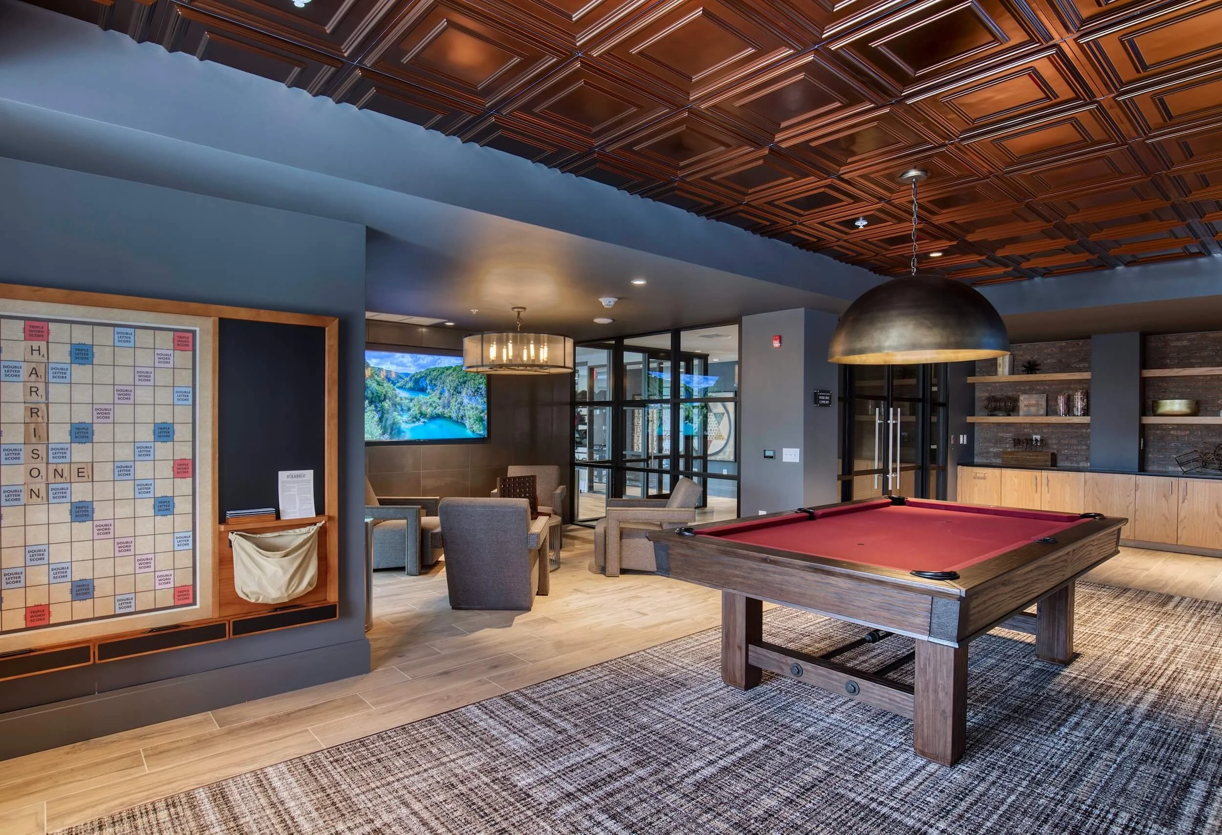 Interior of a lounge area with a pool table, multiple chairs, a wall-mounted TV, and decorative ceiling panels.