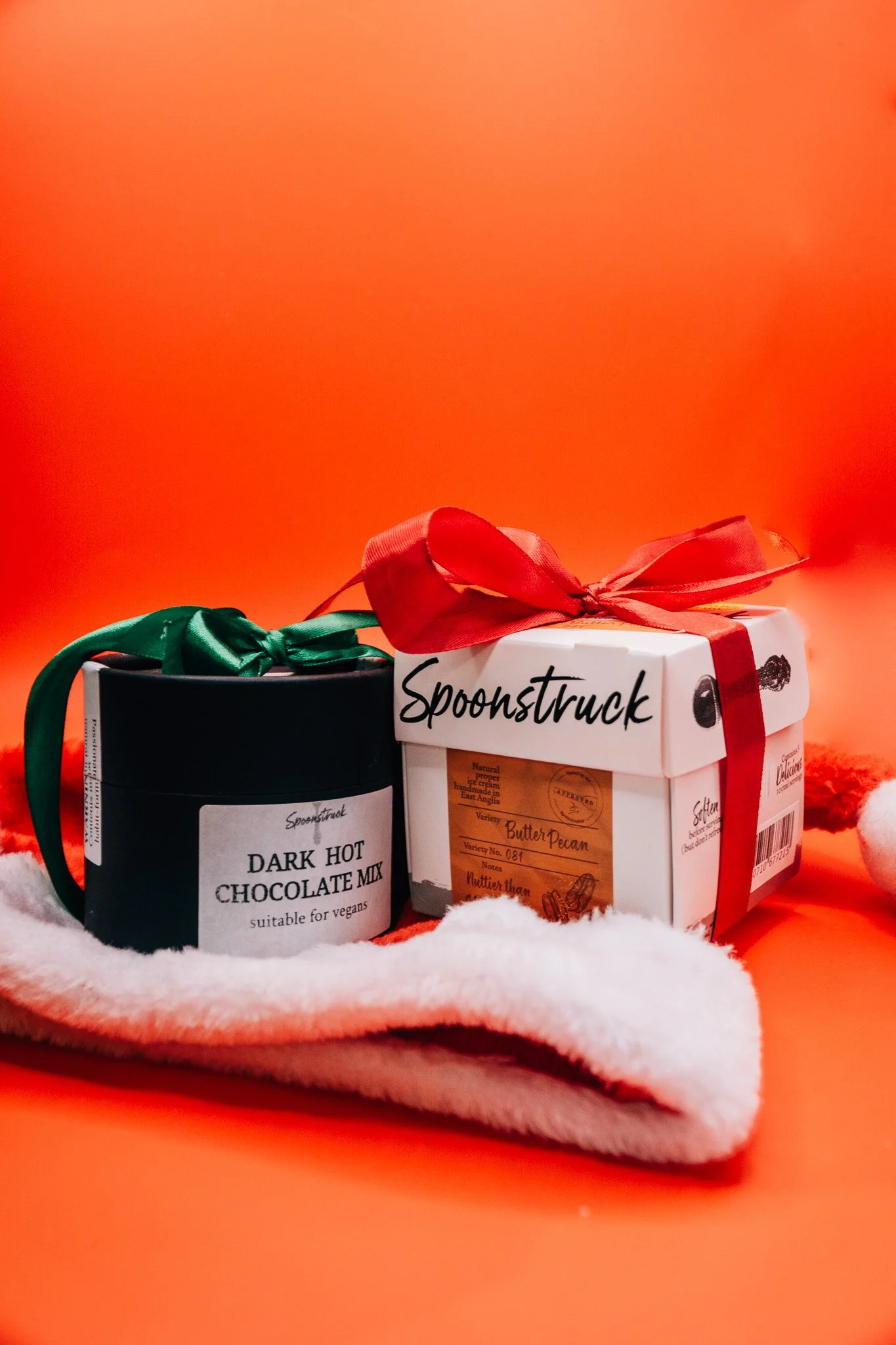Two jars of dessert toppings with bows on a white furry surface against an orange background.