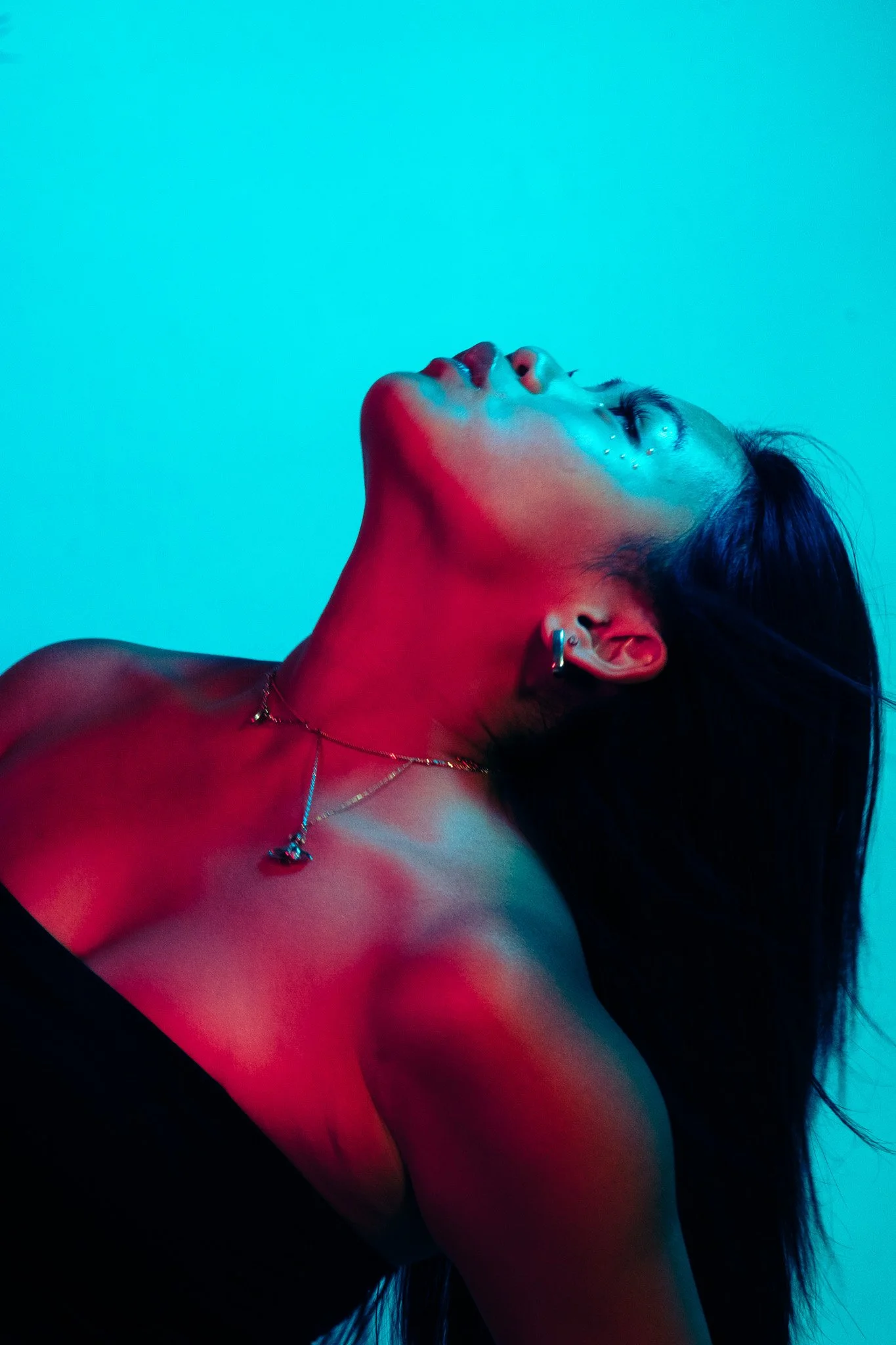 A woman with long dark hair posed with her head tilted back, highlighting her neck and face, with blue and red lighting creating a moody, artistic effect.