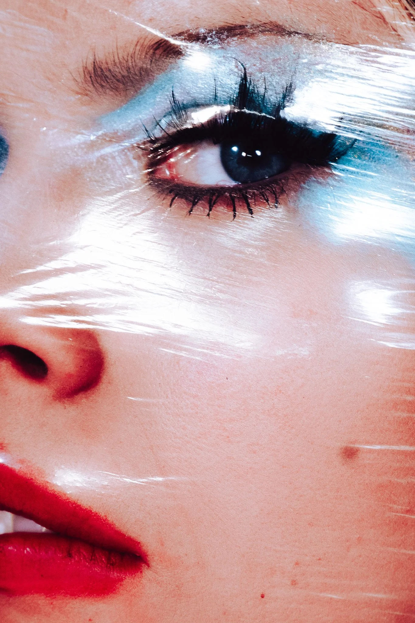 Close-up of a person's eye with makeup, partially covered by a transparent plastic sheet.
