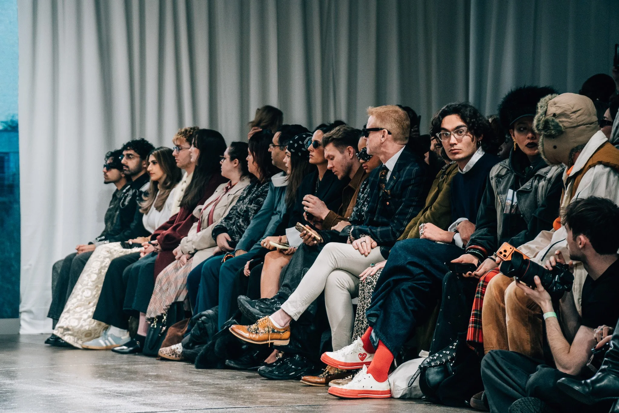 A diverse group of people sitting in a row, attending an indoor event, in front of white curtains.