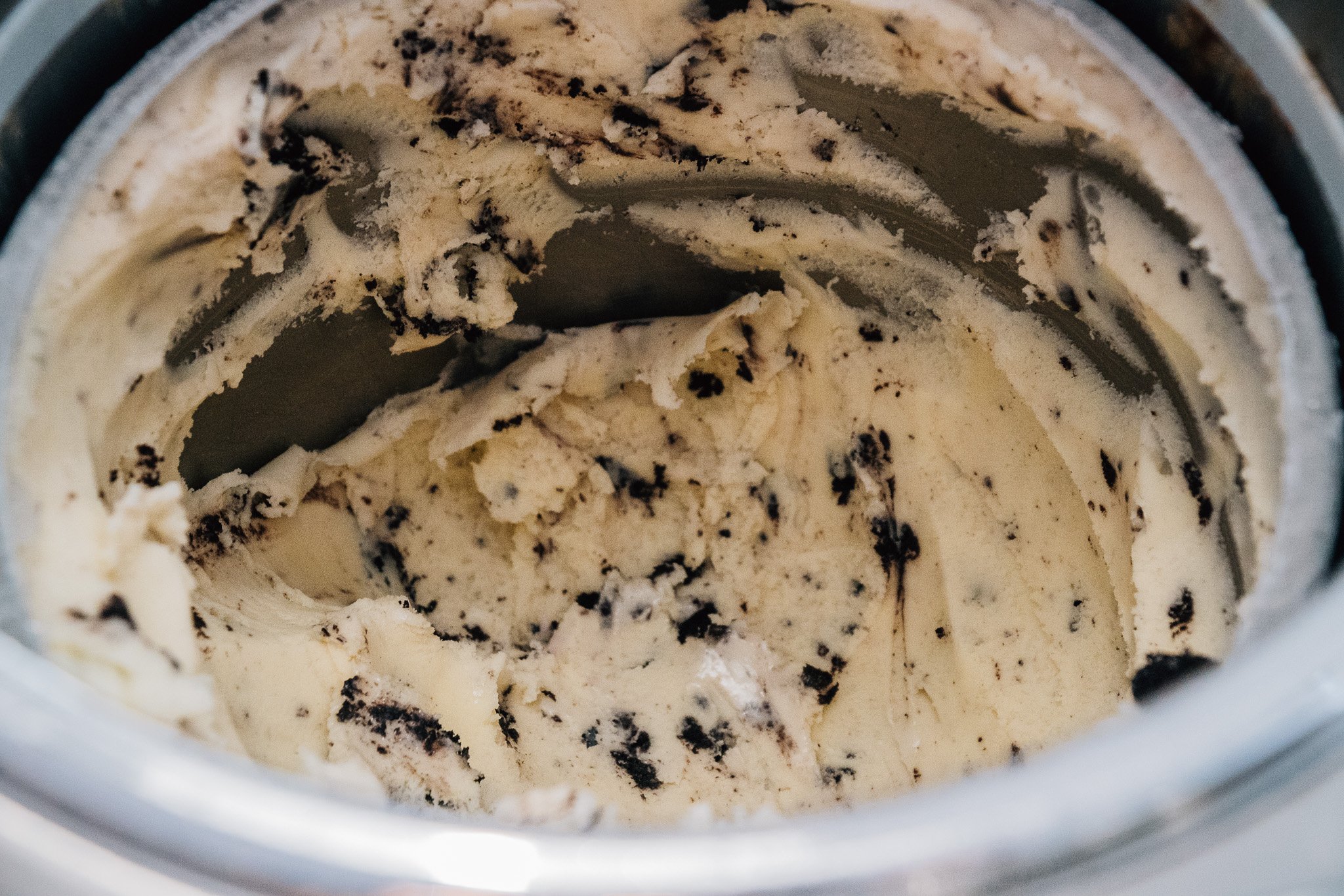 Inside view of a partially empty ice cream container with cookies and cream flavor, showing scoops of vanilla ice cream with chocolate cookie bits mixed in.
