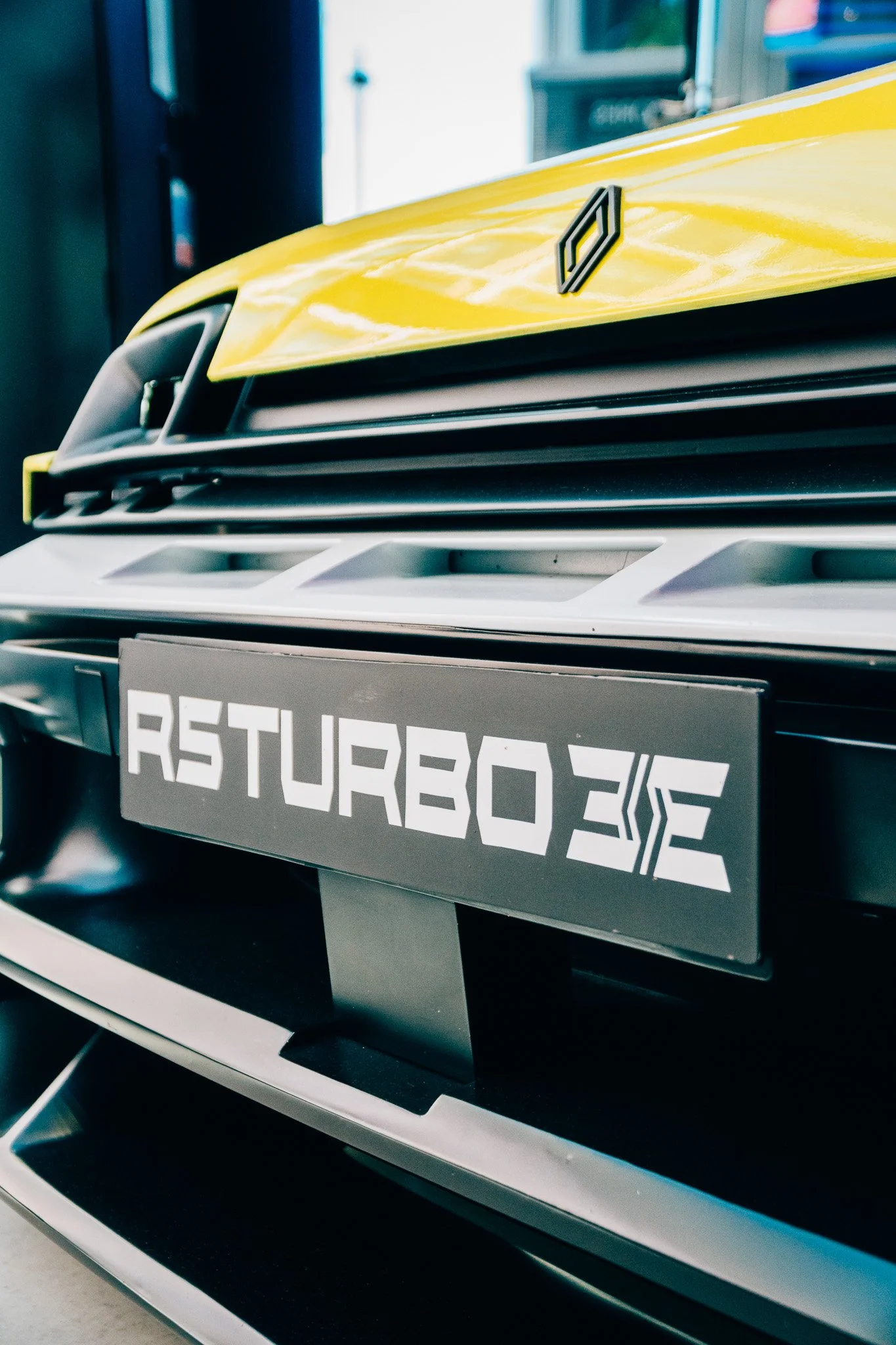 Close-up of a yellow vehicle front with a Renault logo on the hood and a digital display on the grille that reads 'RENAULT 3E'.