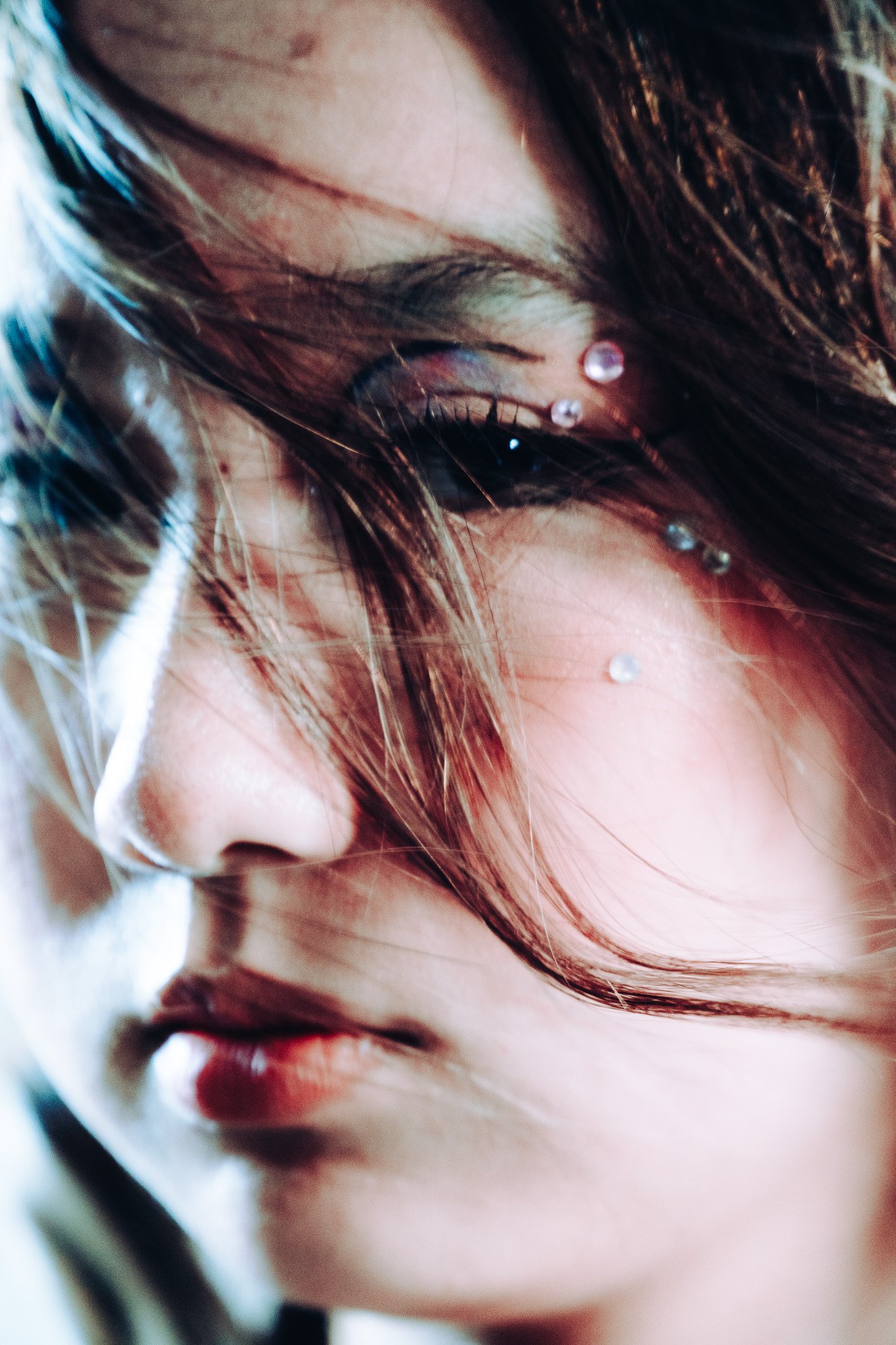 Close-up of a woman's face with wet hair, adorned with small decorative pearls on her face and neck.