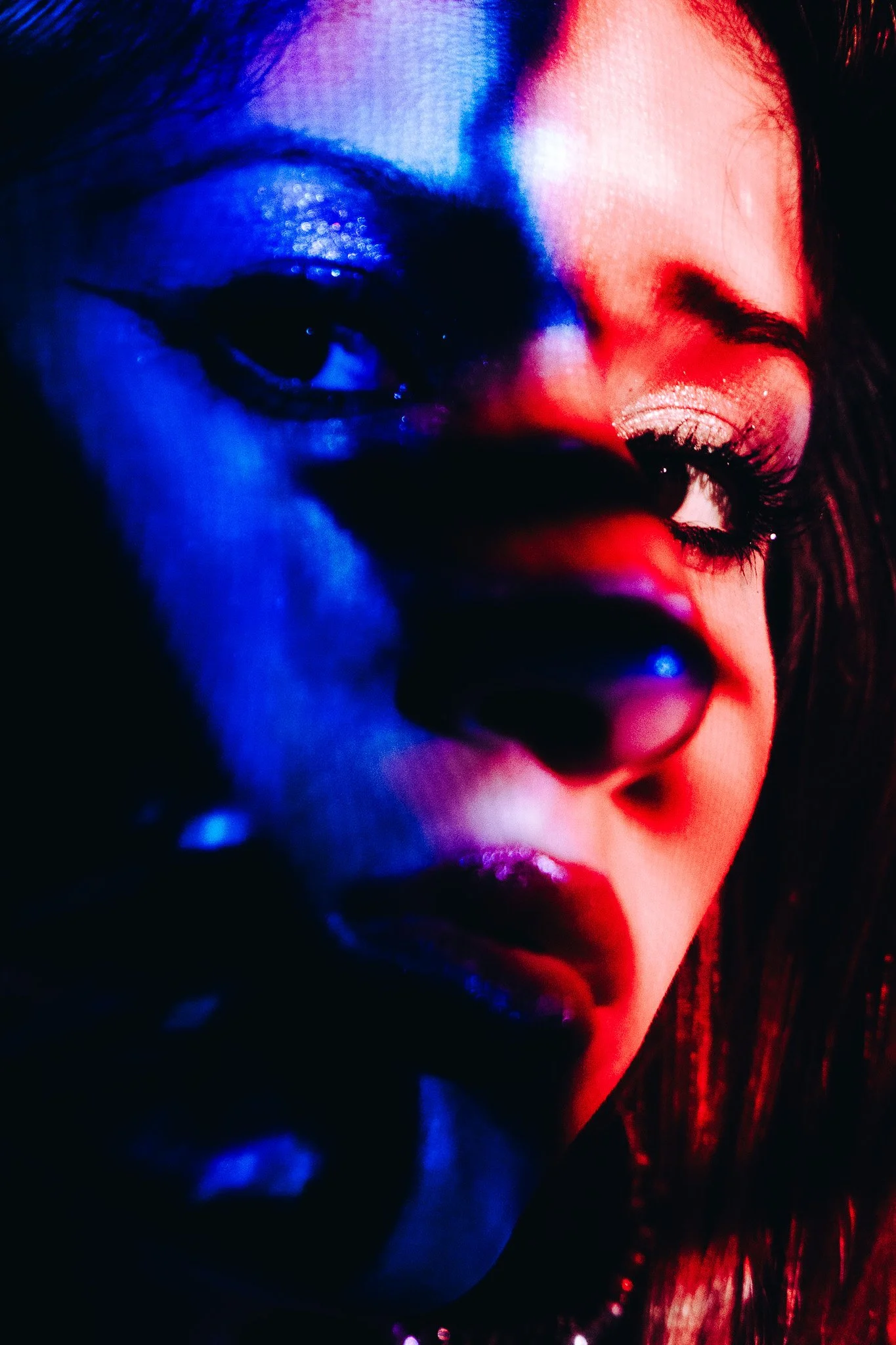 Close-up of a woman's face with vivid red and blue lighting, showing one eye, part of the lips, and dark hair.