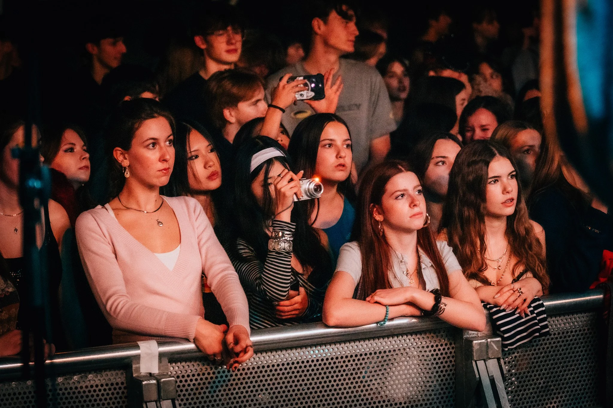 A group of young women and men sitting in the front row at an event, with some taking photos or videos and others watching attentively.