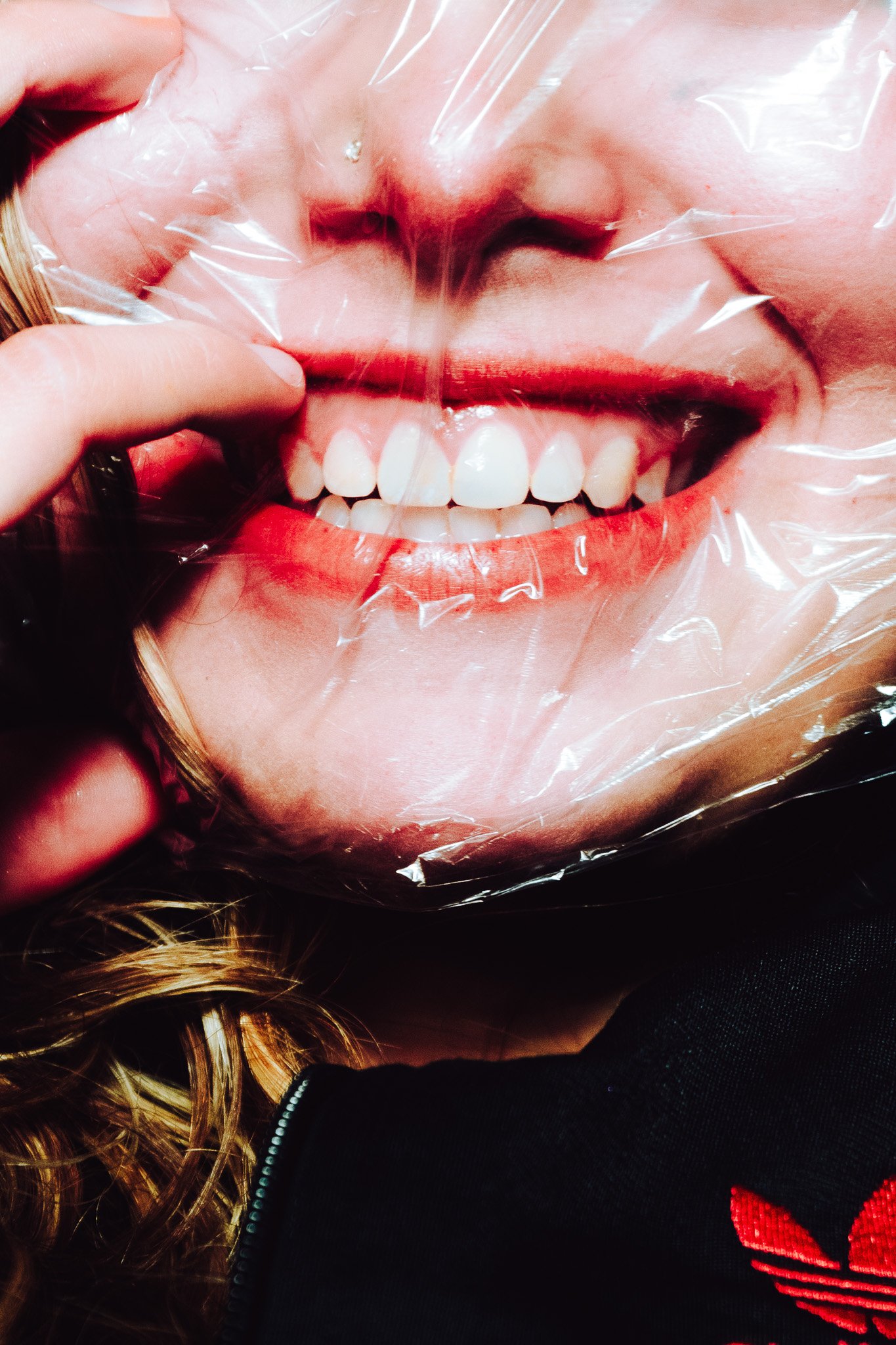 Close-up of a person's mouth smiling, showing teeth, with clear plastic wrap covering part of the face.