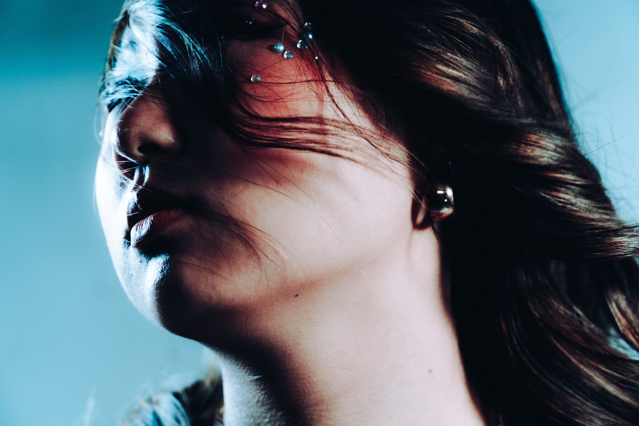 Close-up of a woman's face with dark brown hair, some strands falling over her closed eyes, and drops of water on her hair.