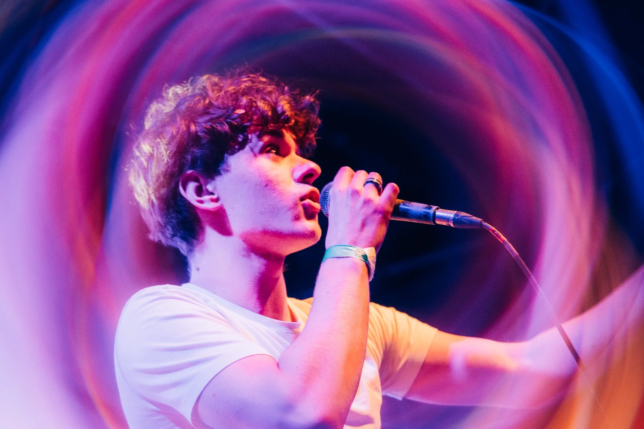 A person singing into a microphone on stage with colorful, blurred lights in the background.