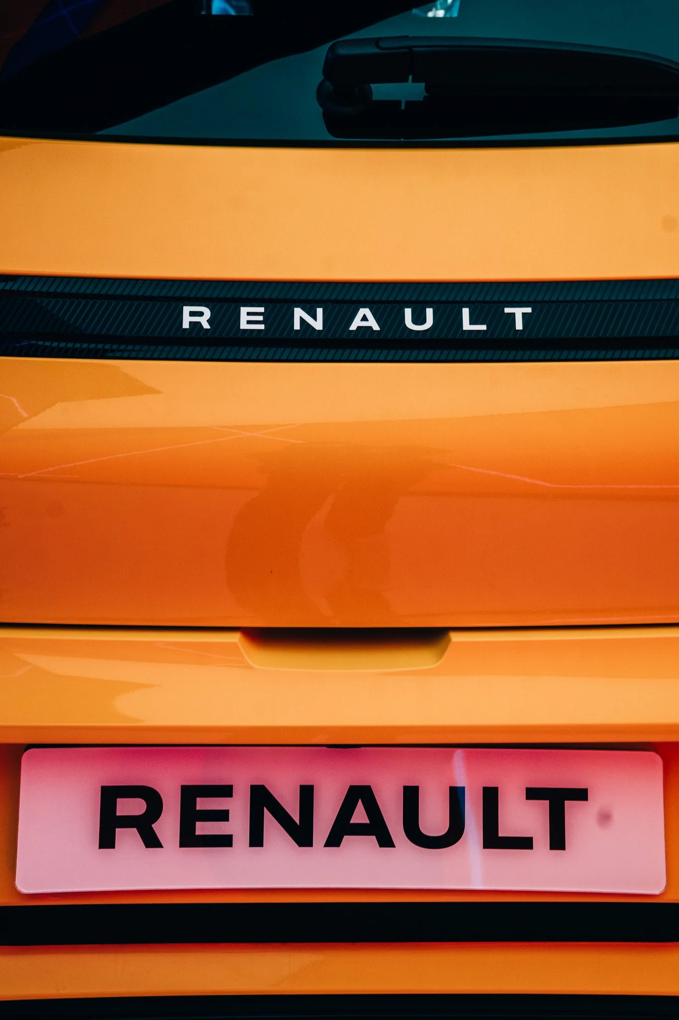 Close-up of Renault vehicle with visible front grille, orange exterior, and a pink parking permit with black text reading "RENAULT."