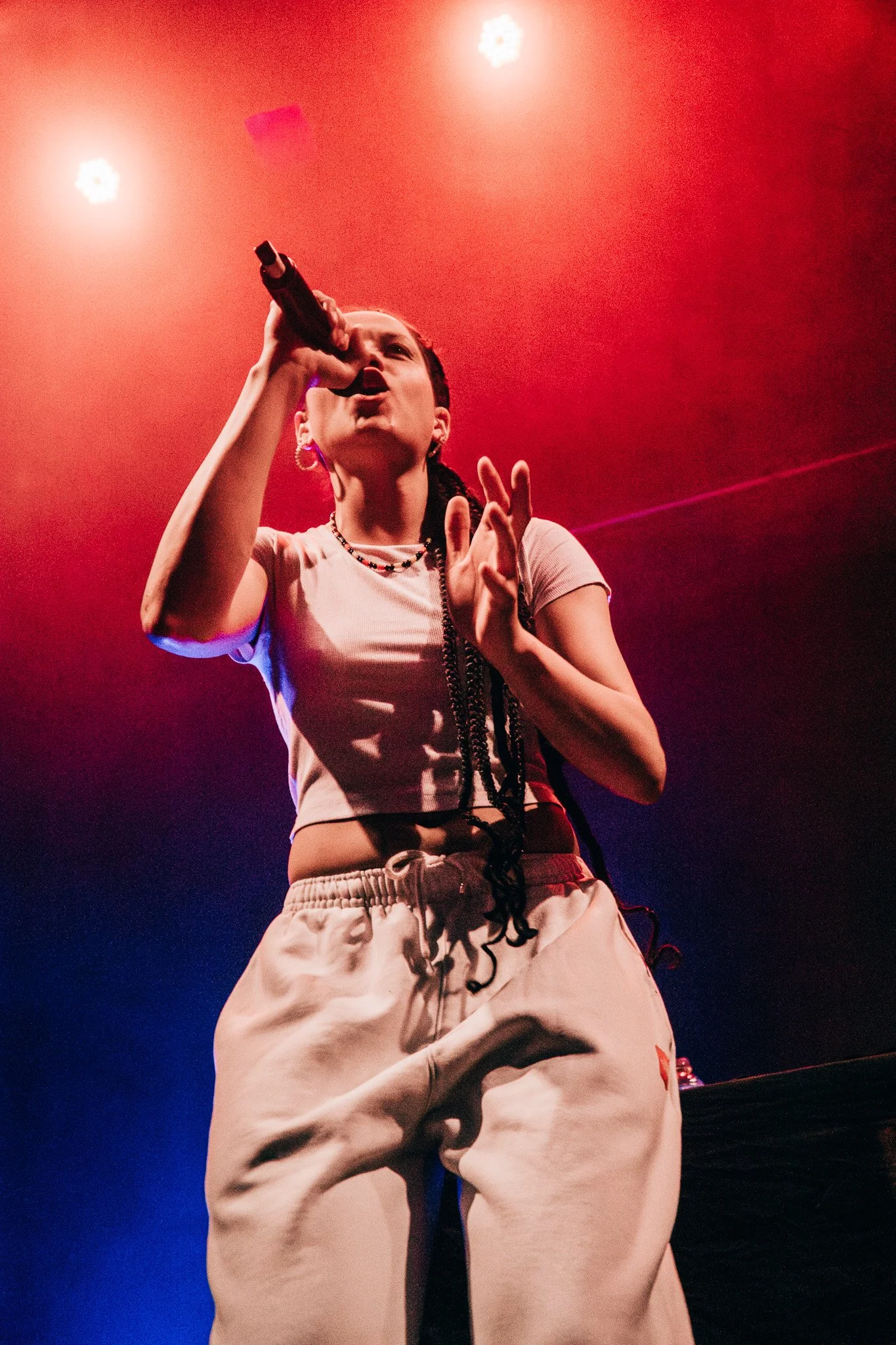 Woman singing into a microphone on stage with red and blue lighting.