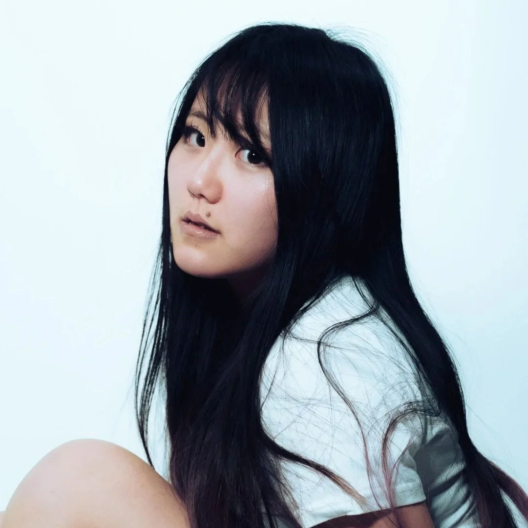 Portrait of a young woman with long black hair looking at the camera against a plain white background.