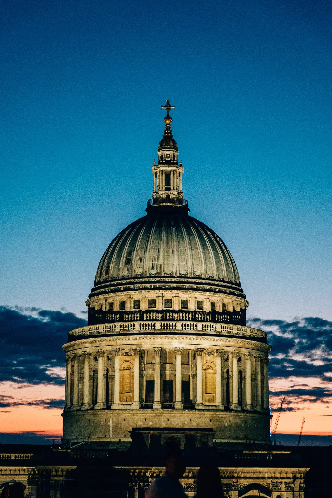The dome of St. Paul’s Cathedral with a cross on top under a dusk sky, people silhouetted in front.