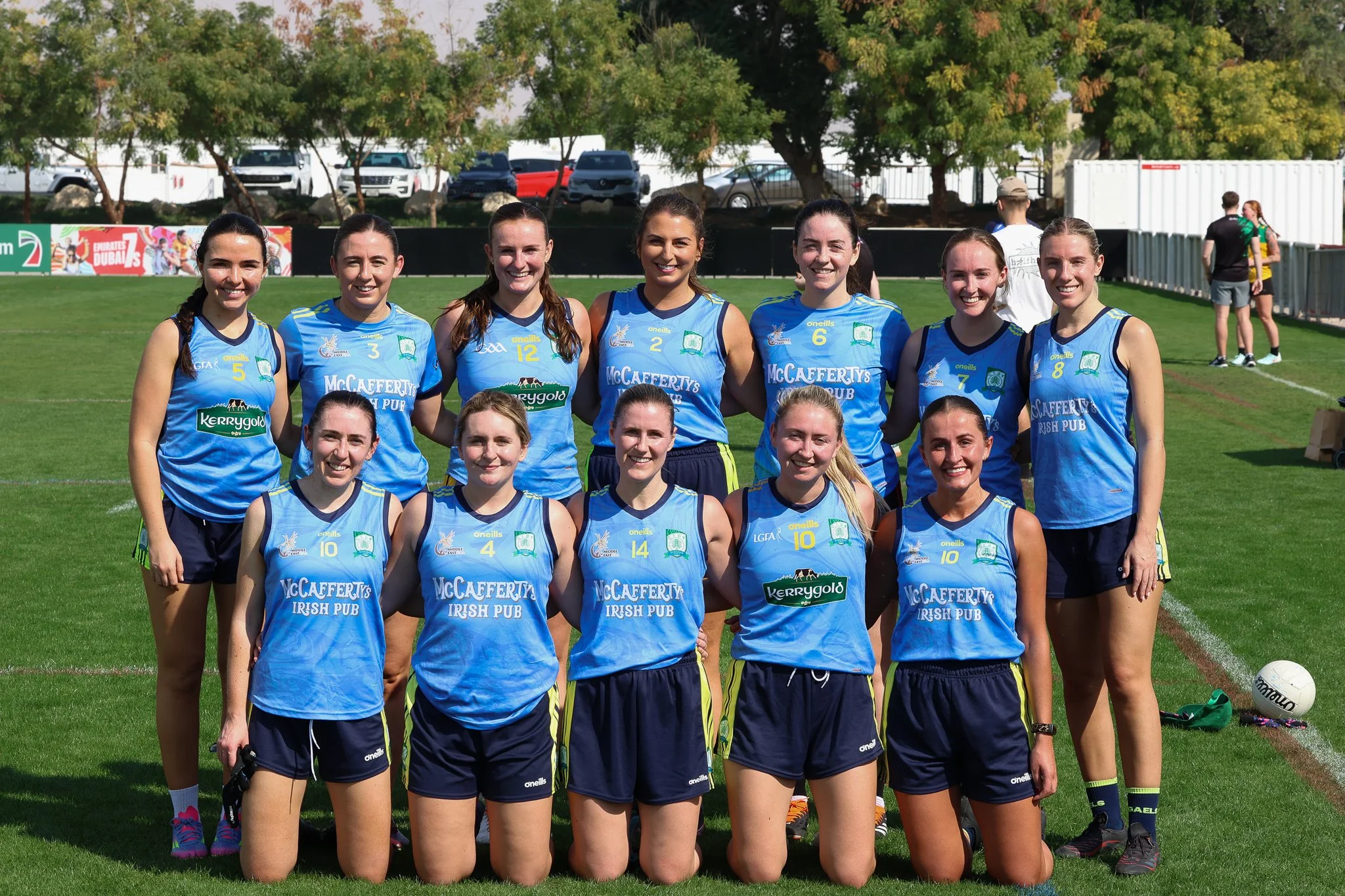 Group of female athletes in blue sports uniforms posing on a grassy field.