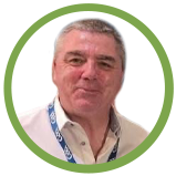 A middle-aged man with gray hair smiling, wearing a collared shirt and a lanyard, standing against a white background with a green circular border.