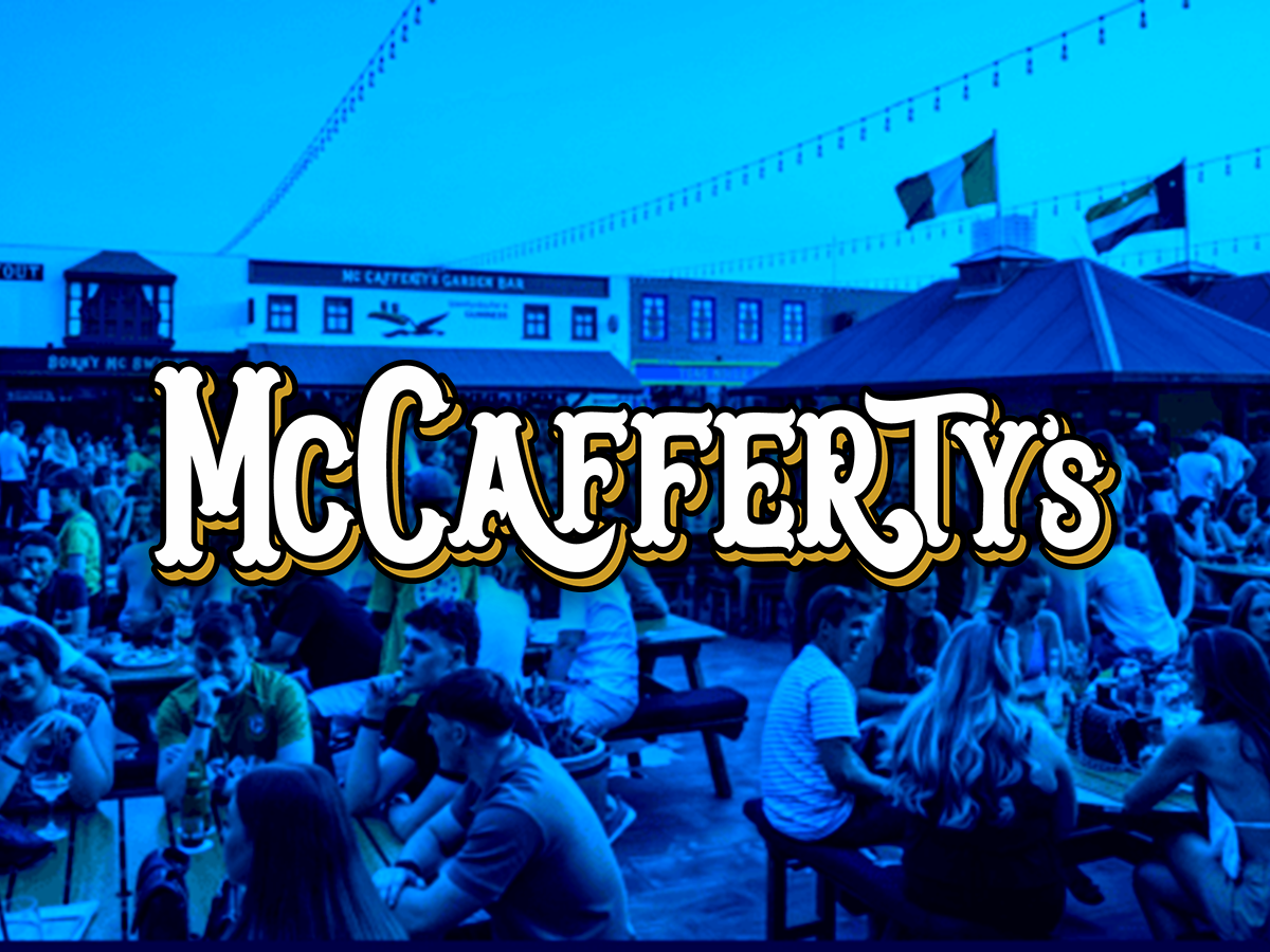 Crowd of people sitting at outdoor tables at McCafferty's Bar during evening, with flags and string lights overhead
