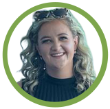 Smiling woman with curly blonde hair wearing a dark sweater, in a green circular frame