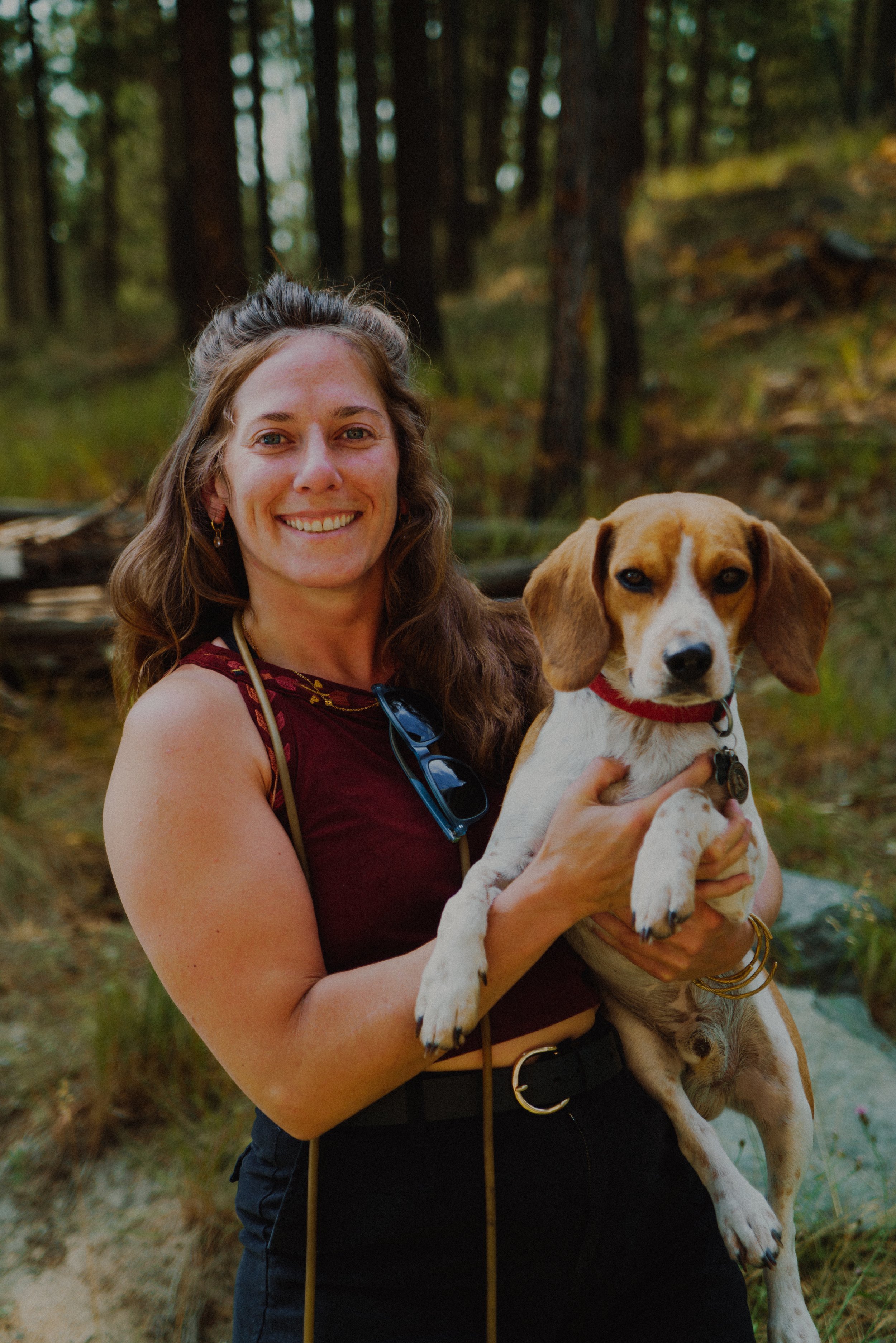 Glass blowing artist, Paris of Sweet P. & Things smiling and holding a beagle puppy in a forest setting.