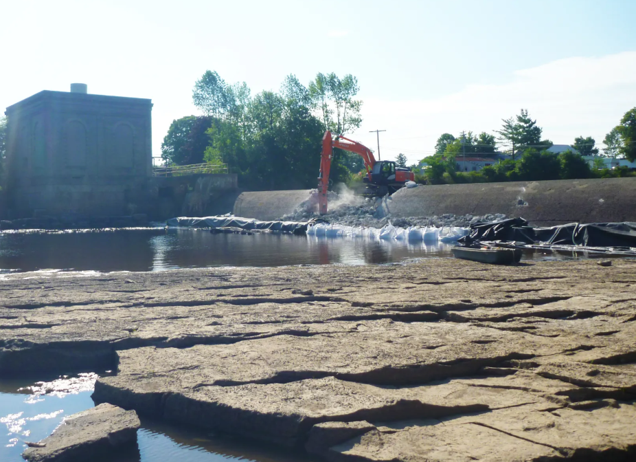 Construction equipment working on a water management project on a dry riverbed during daytime.