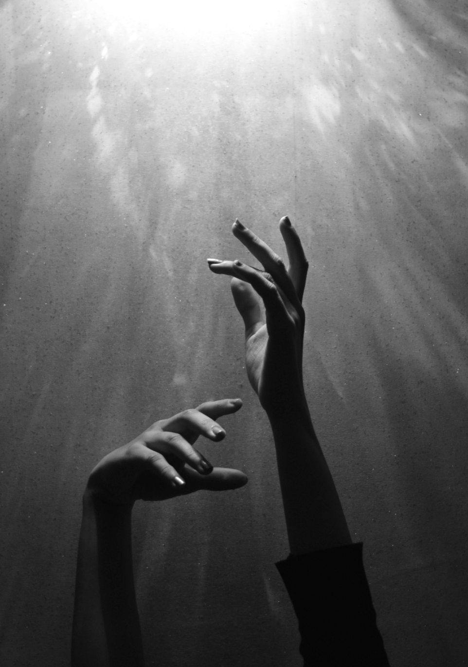Black and white photo of two hands reaching up in front of a diffused light source on a textured surface.