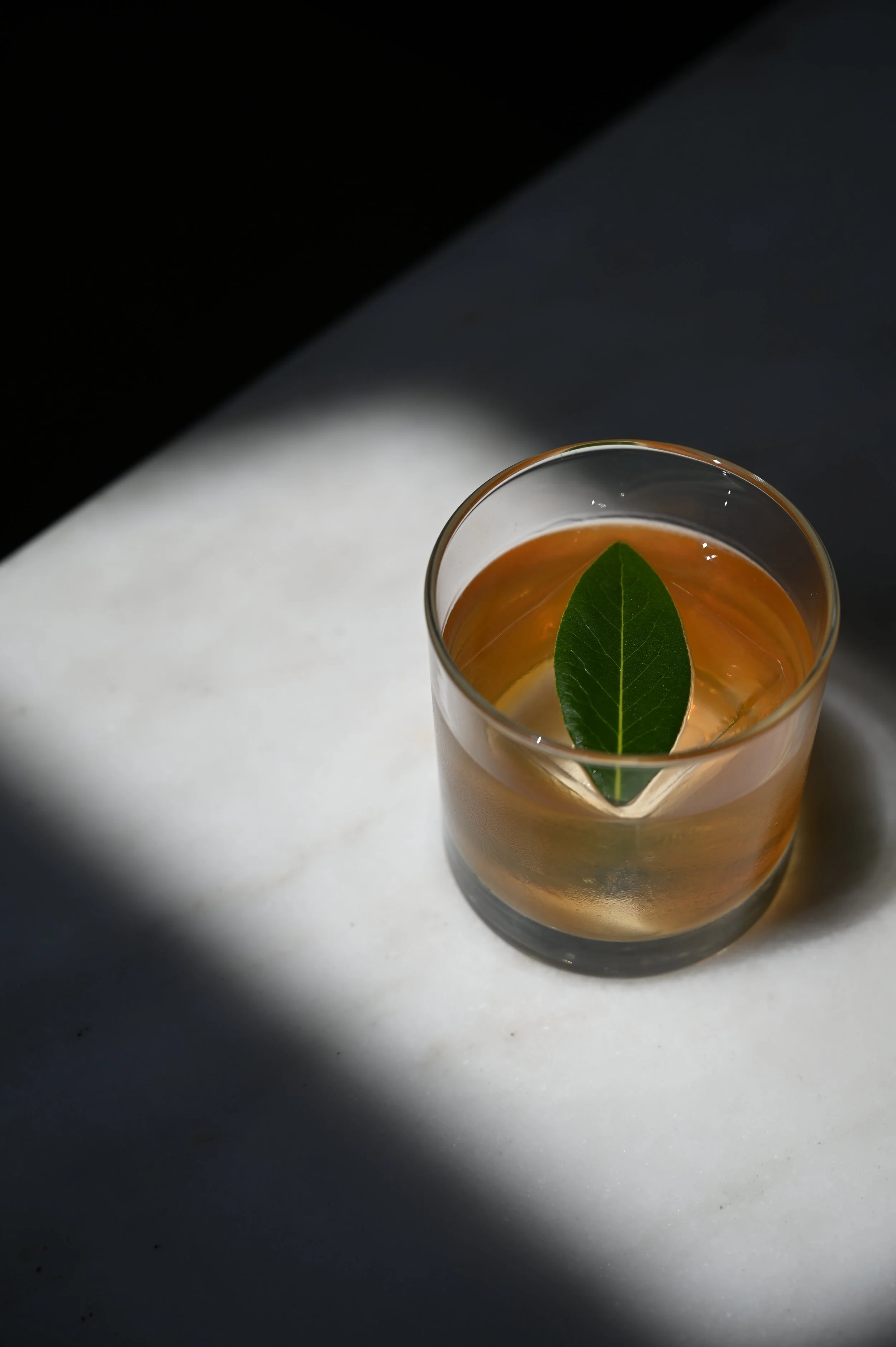 A glass of iced tea with a green leaf inside, on a black and white surface with shadowed lighting.