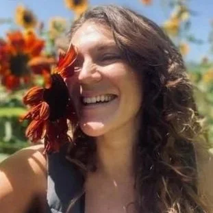 Woman smiling outdoors surrounded by colorful flowers.