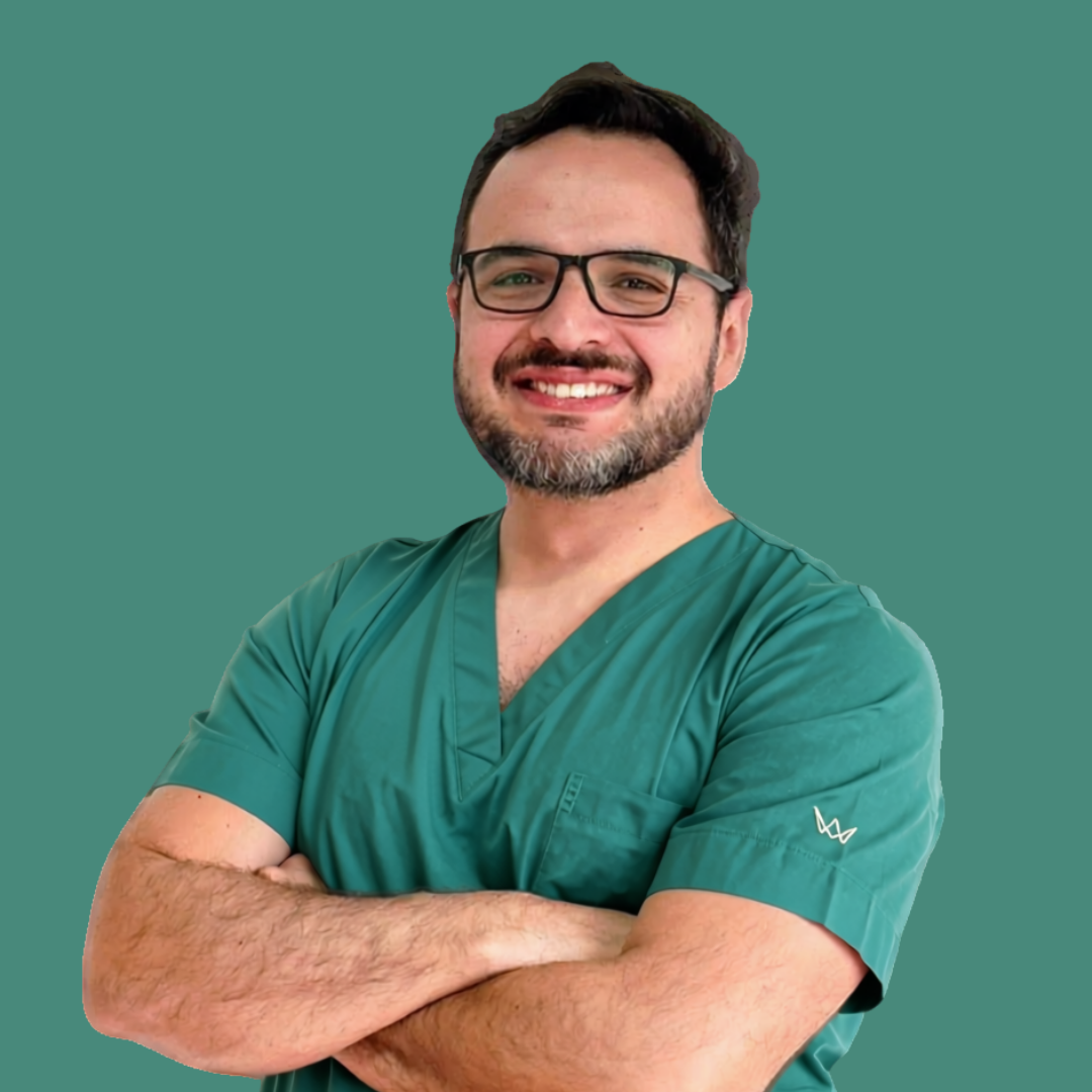 Hombre con barba, gafas y bata de trabajo sonriendo con los brazos cruzados, fondo verde.