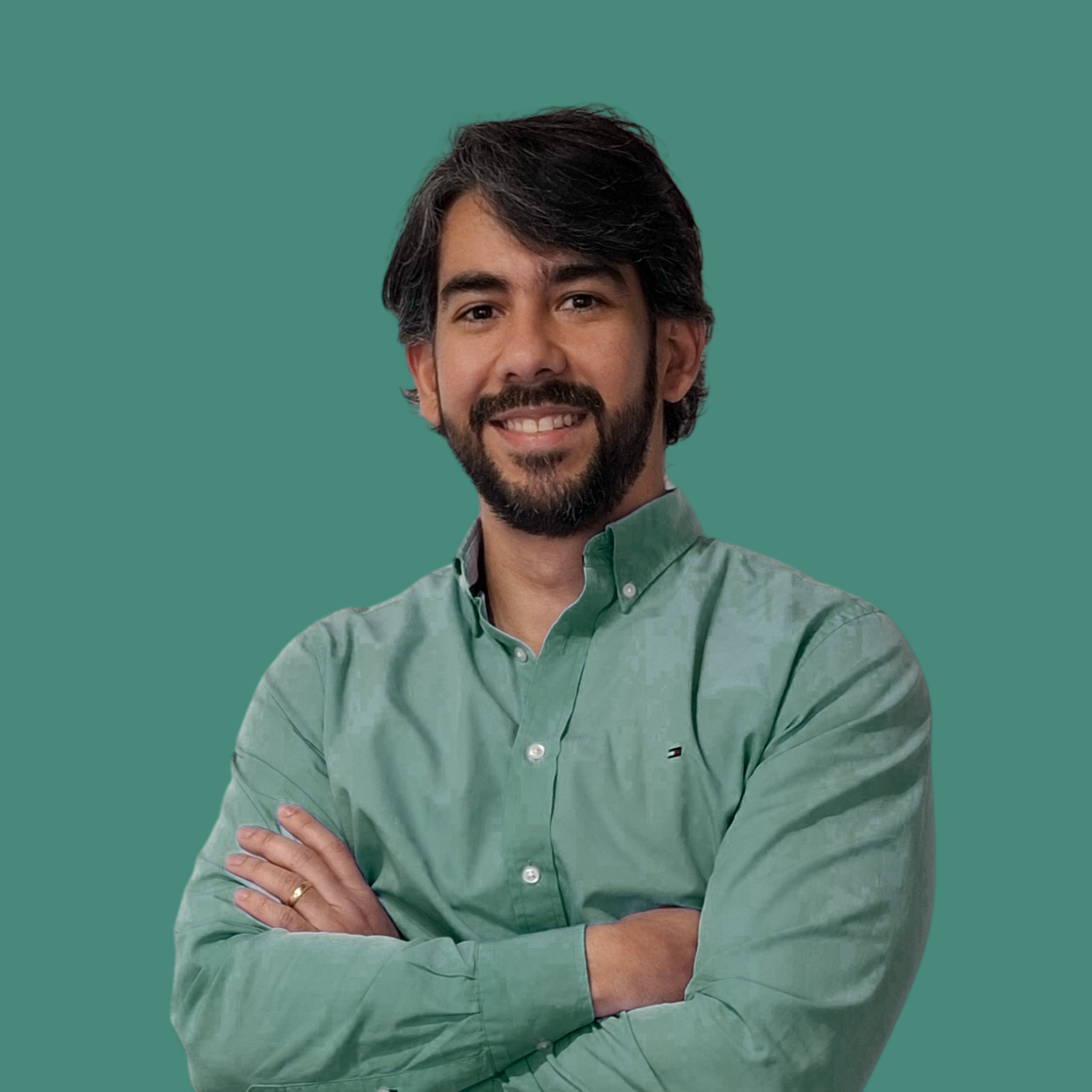 Hombre de cabello oscuro y barba, sonriendo y con los brazos cruzados, vestimenta de camisa de color verde y fondo verde