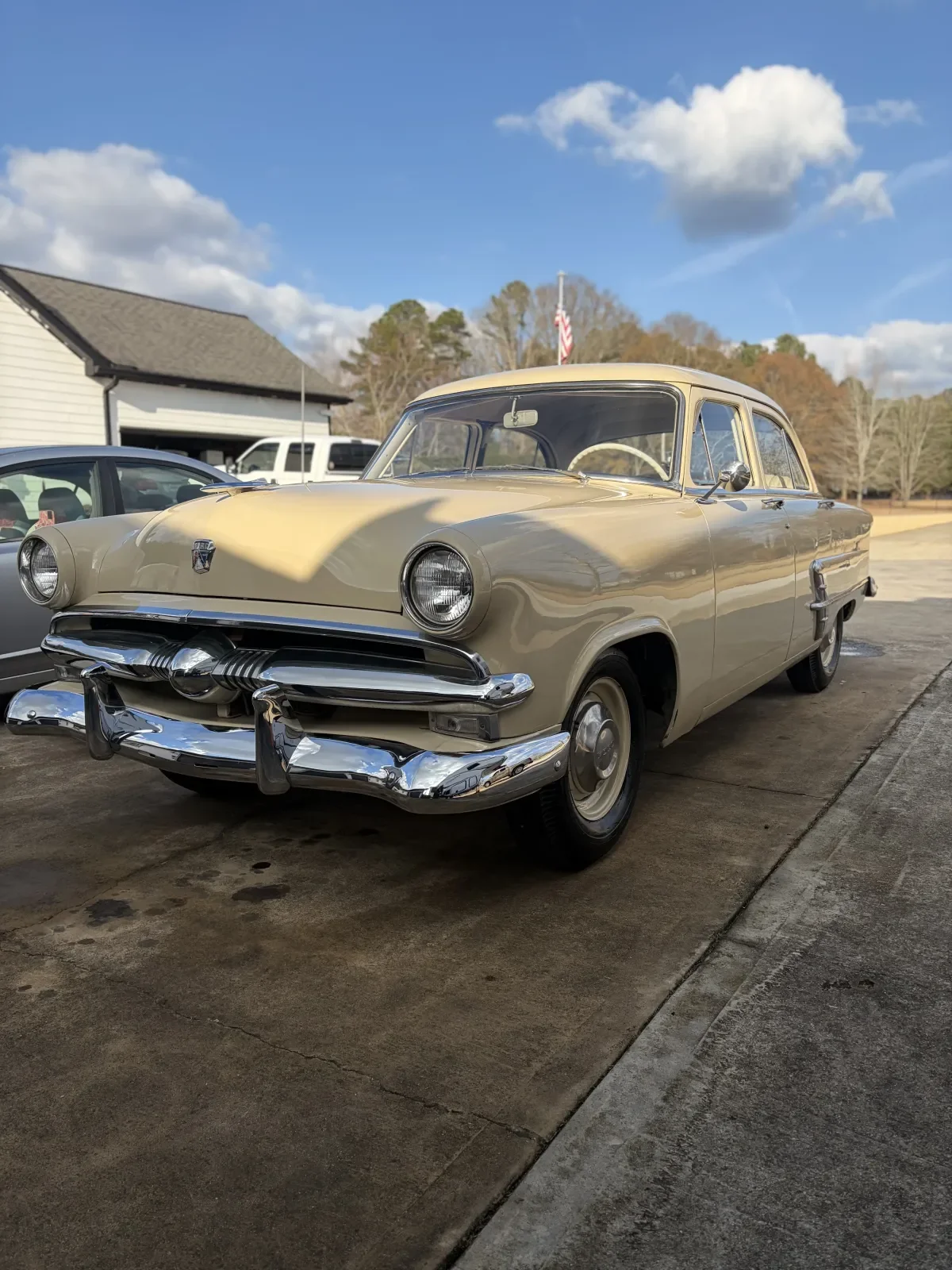 A vintage beige car parked on a driveway with a blue sky and some clouds overhead.