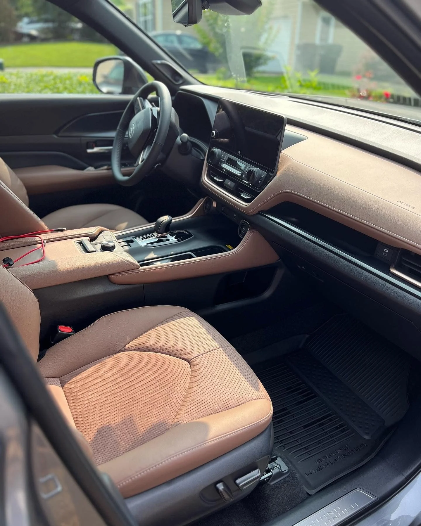 Inside view of a Toyota Highlander showing the tan leather seat, dashboard, steering wheel, and gear shift.