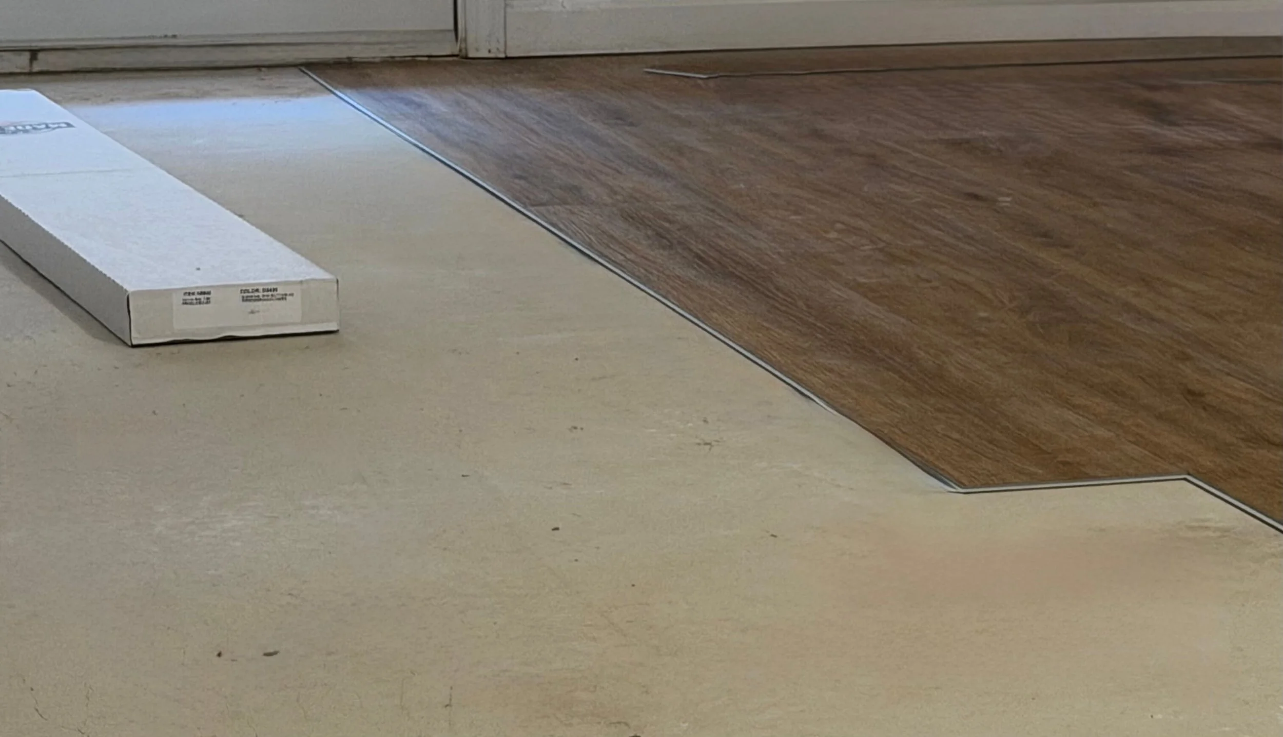 Close-up of a beige and brown tiled floor near a door, with a white box on the floor.